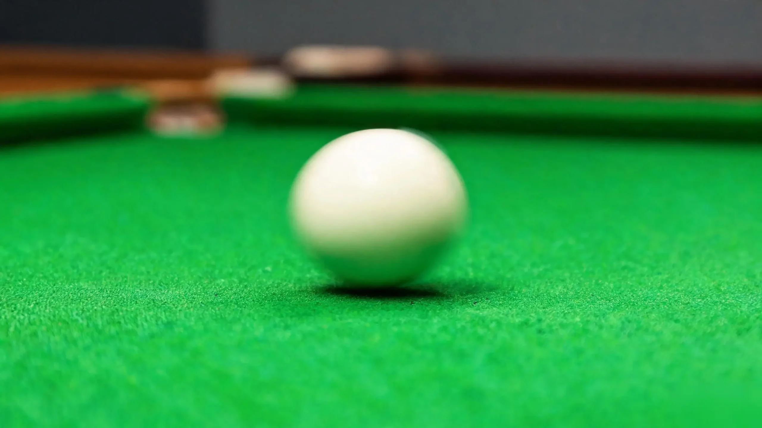 White billiard ball rolling across the green cloth surface in motion with low camera angle