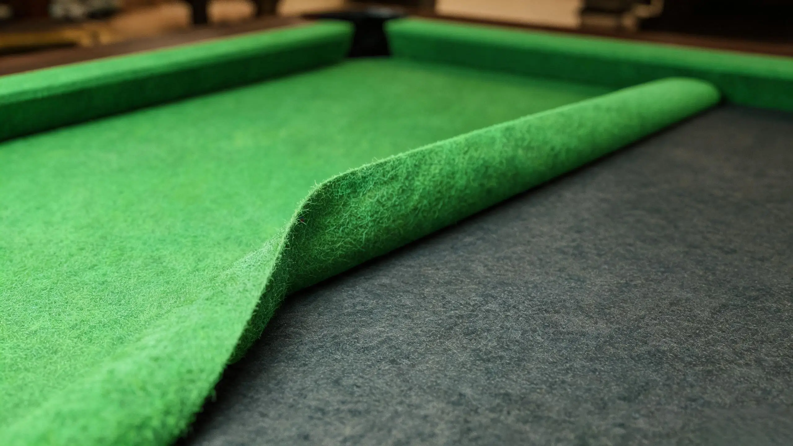 Corner of green billiard cloth lifted back to reveal the dark slate bed underneath