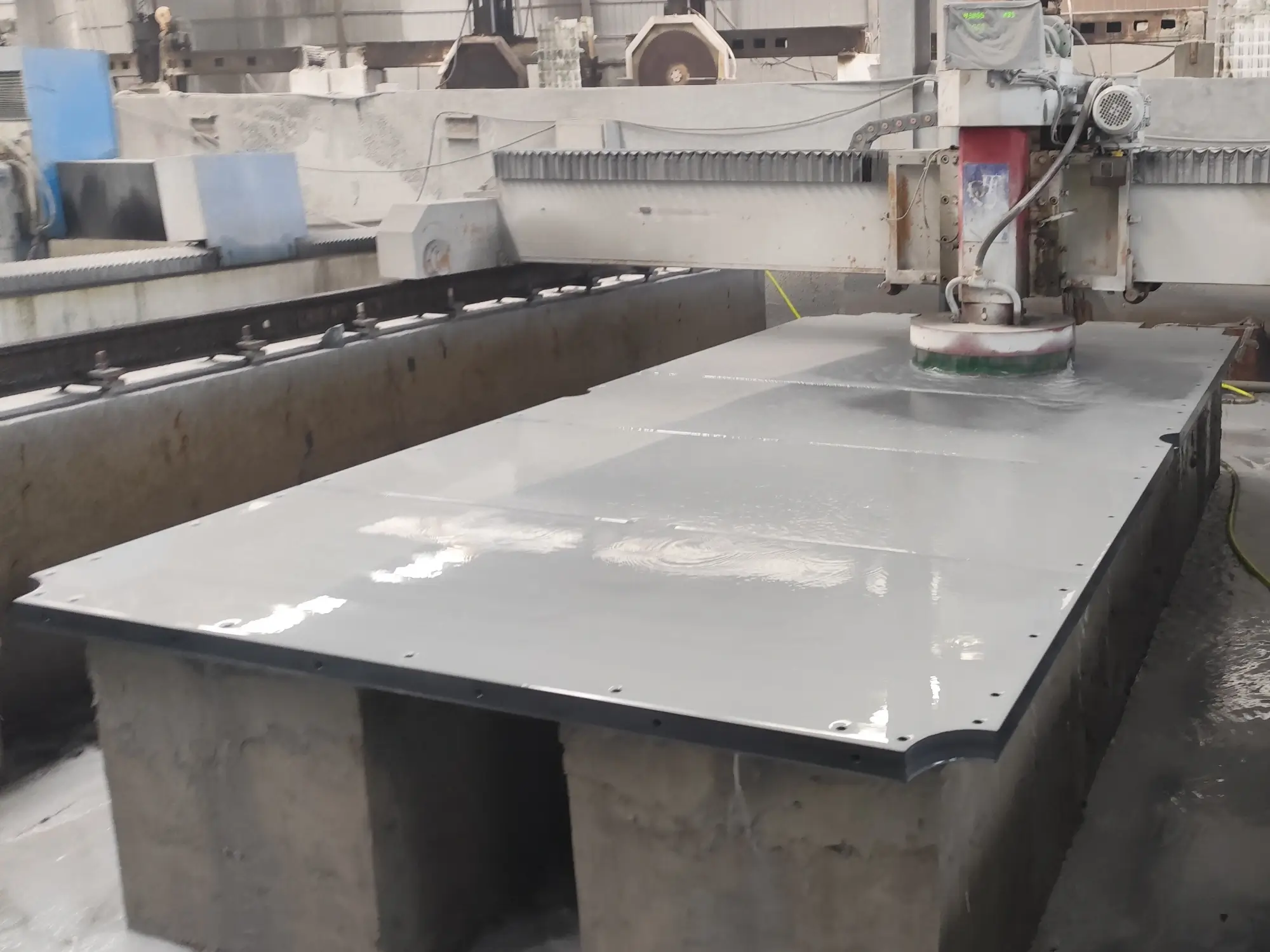 CNC machine precision-machining a large dark grey slate panel for a billiard table bed in a factory