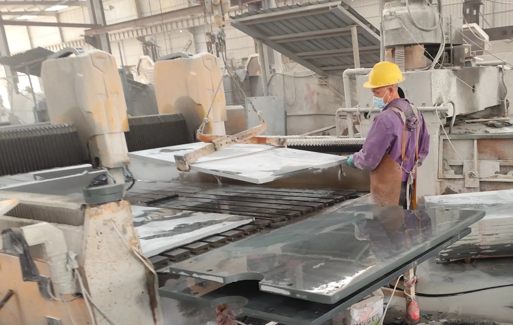 CNC operator in safety gear observing a slate panel machining through the closed door