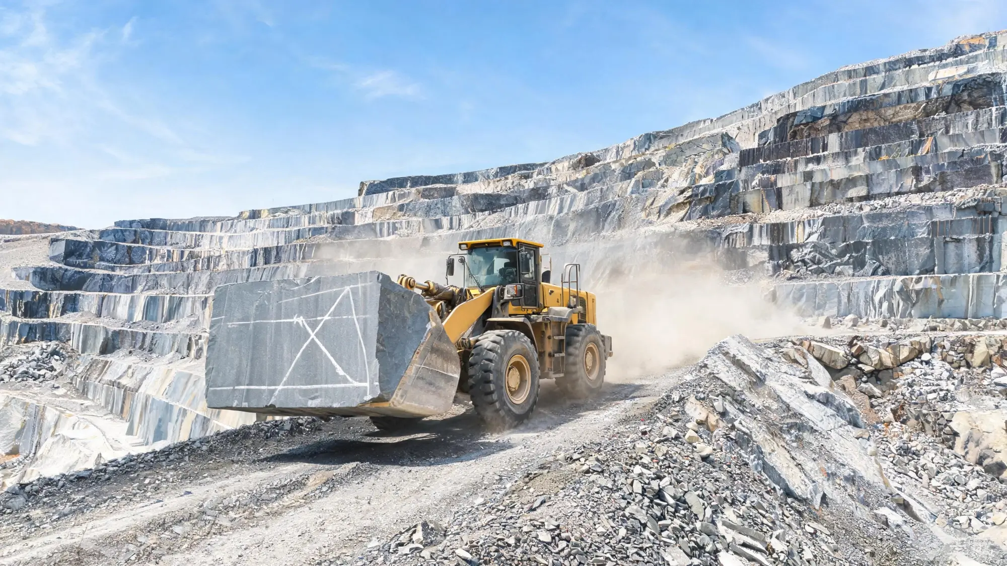 Moving extracted slate blocks from quarry face to storage yard Front loader carrying a large rectangular slate block down a quarry ramp