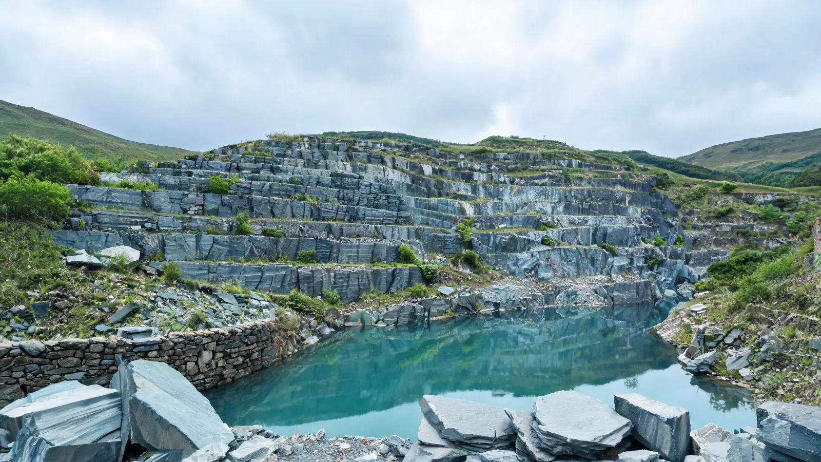 Lushan, Xingzi and the Slate Belt of Jiangxi 2 Historic hand-worked slate quarry in the Lushan foothills near Xingzi — stepped benches of grey-blue slate, thin rock layering on the weathered face, grassed rubble and a rainwater pool