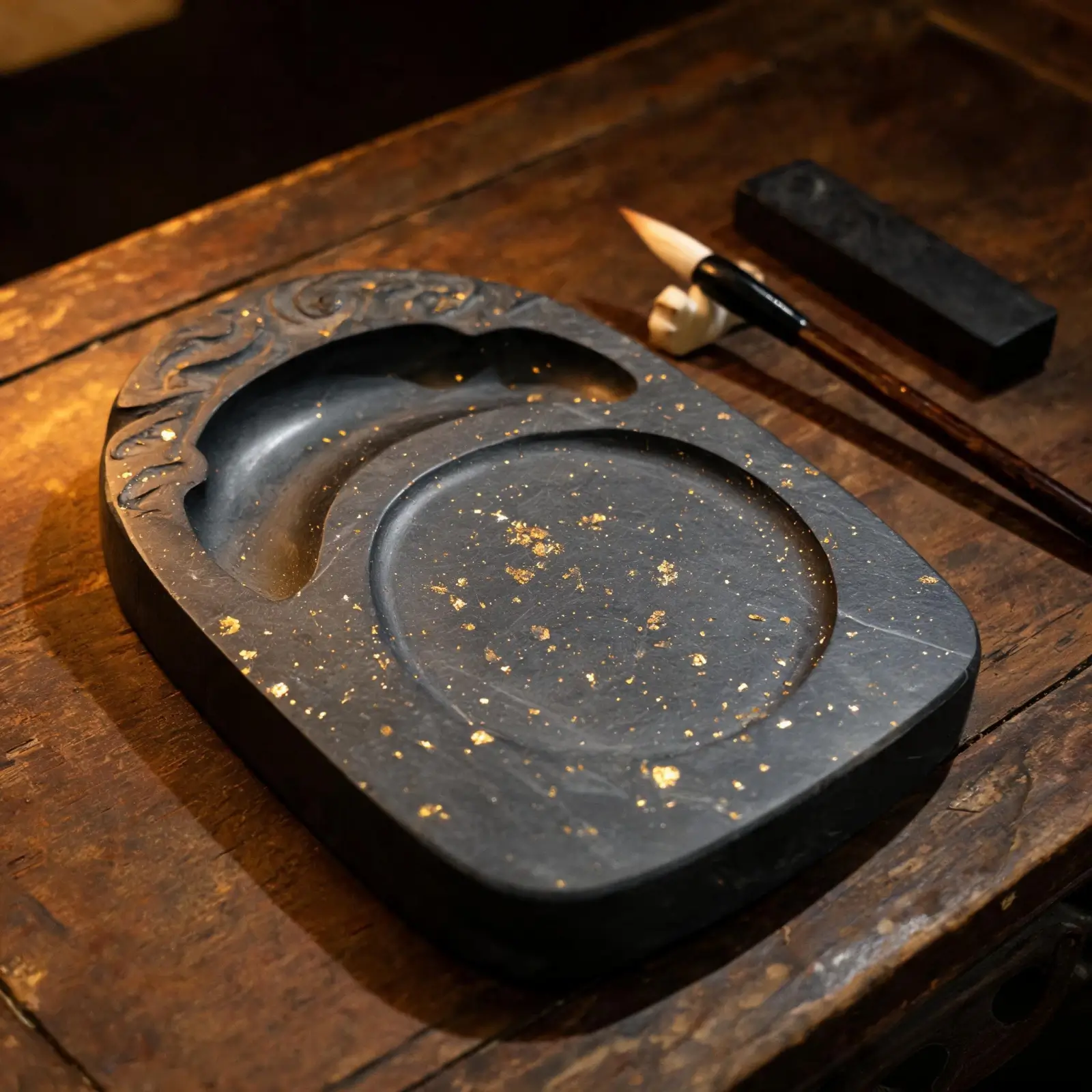 Traditional Chinese Jinxing gold-star inkstone made from dark Jiujiang slate with golden pyrite crystal inclusions, beside a calligraphy brush and ink stick