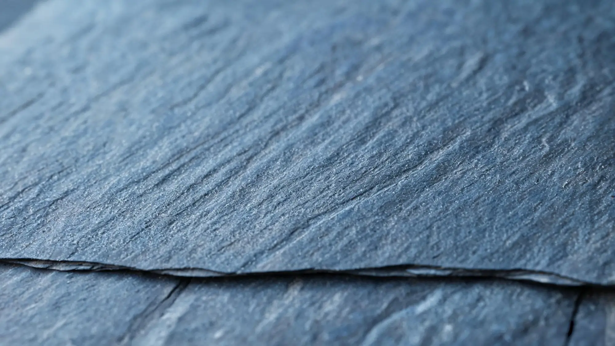 Macro close-up of the natural cleft surface of Jiujiang slate showing fine grain and faint sediment ripple lines