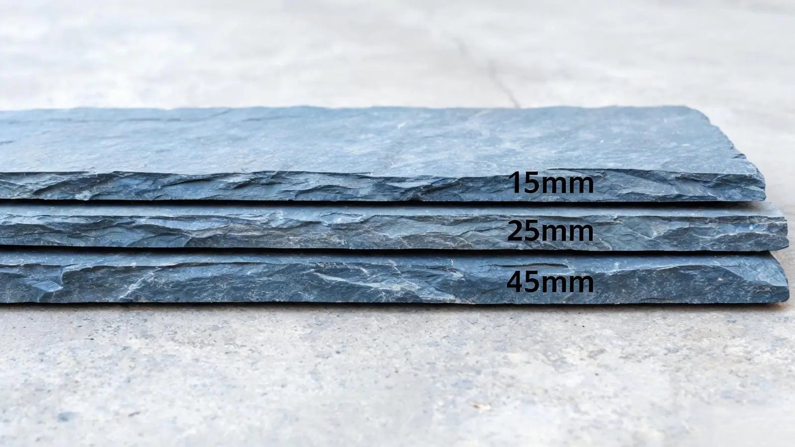 Jiujiang Slate Density 6 Three blue-grey slate slabs of different thicknesses stacked flat on a concrete floor, showing 15mm, 25mm and 45mm profiles