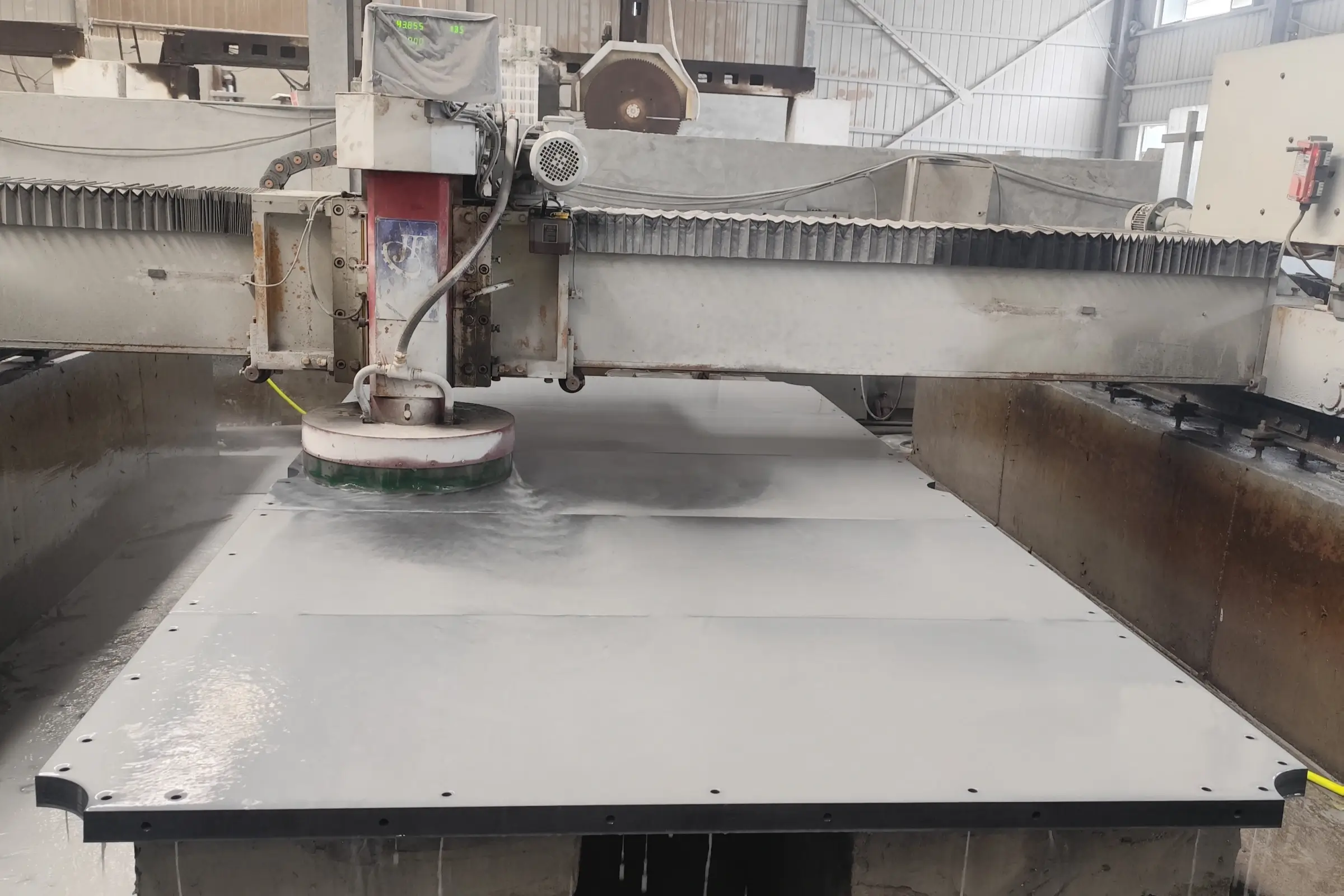 Jiujiang Slate Flatness & Dimensional Stability 2 A CNC machine grinding the surface of a large dark grey slate billiard bed panel with coolant spray in a factory workshop