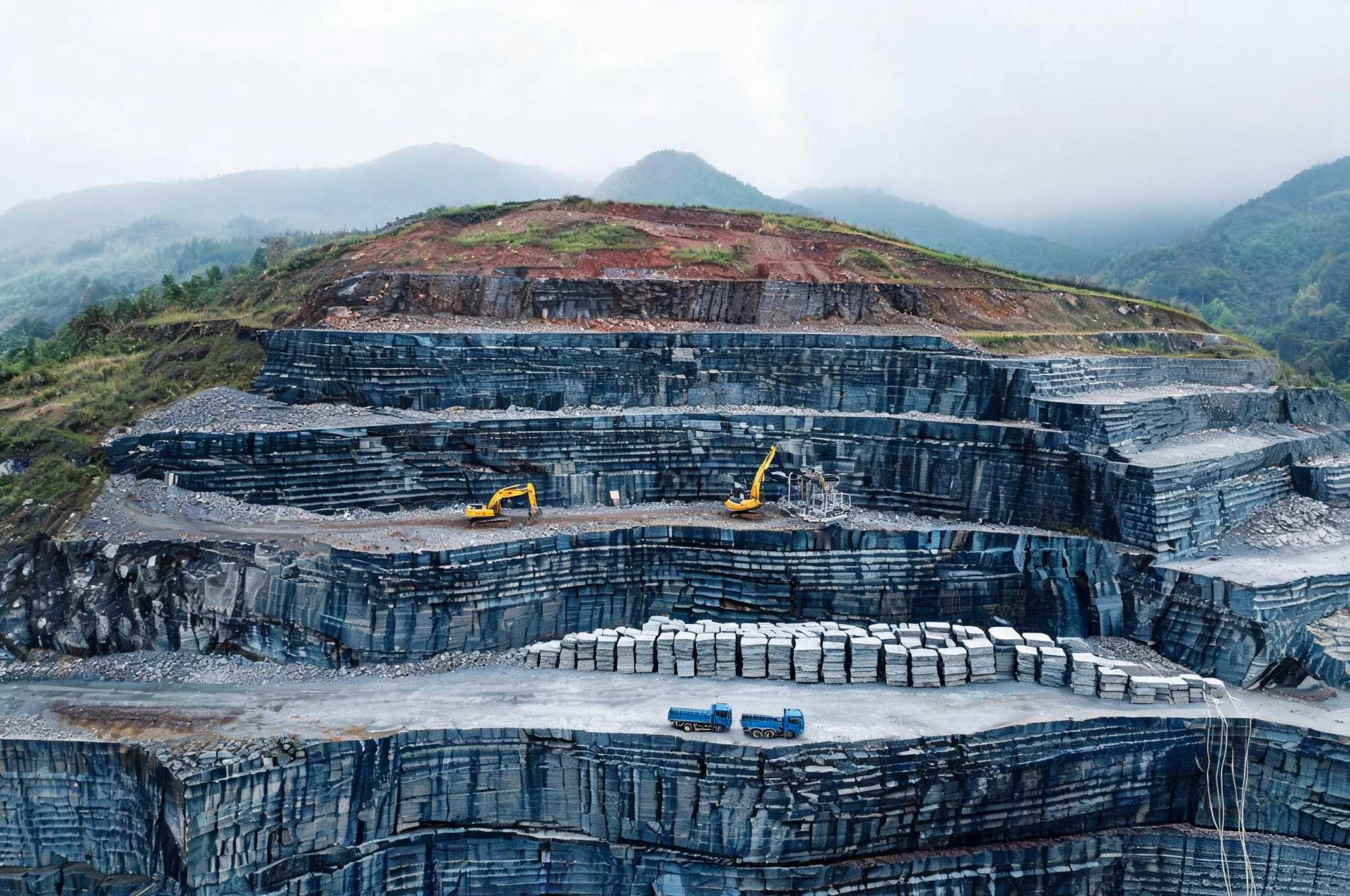 Jiujiang Slate Resources and Quarry Reserves 1 Open-cast slate quarry in the Jiujiang belt with stepped benches cut into thick grey-blue beds, terraced working faces under a hazy sky