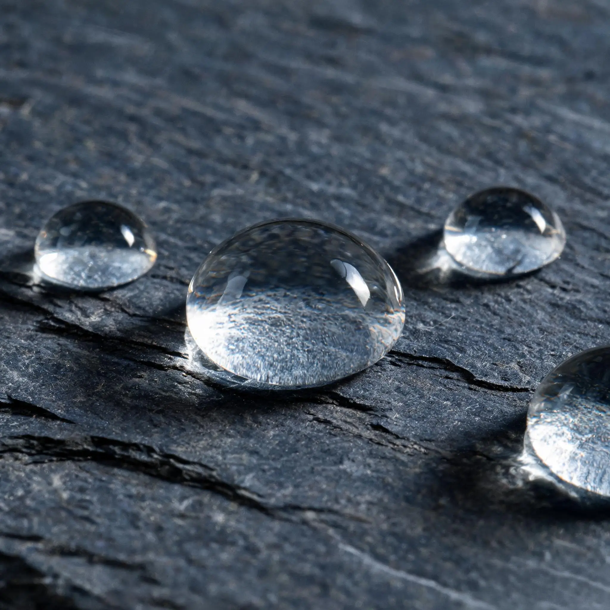 Jiujiang Slate Water Absorption 3 Clear water droplets beading up tall and round on a dark grey slate surface, demonstrating very low water absorption