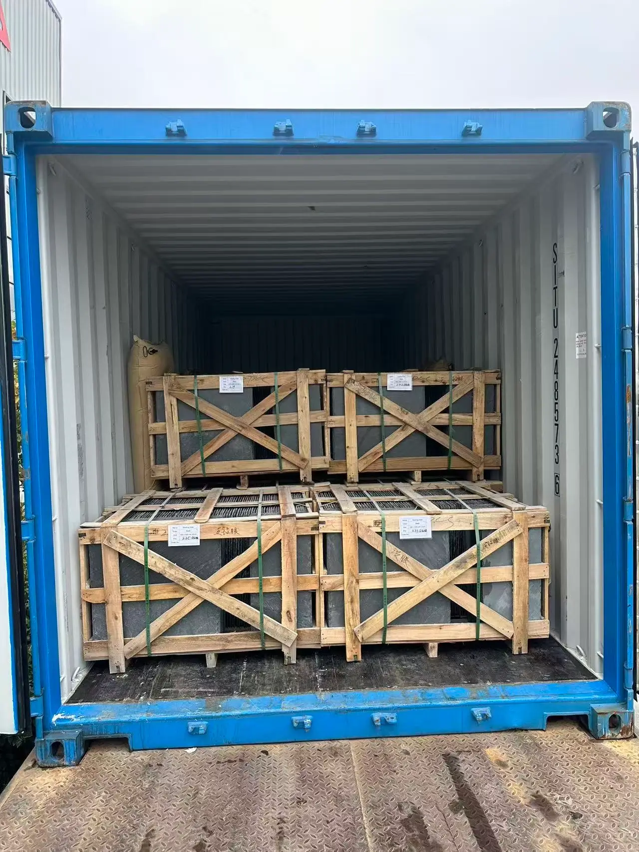 Loaded slate container photographed before the doors close Shipping container with one door open and one half closed showing the last wooden slate crates stacked inside before sealing