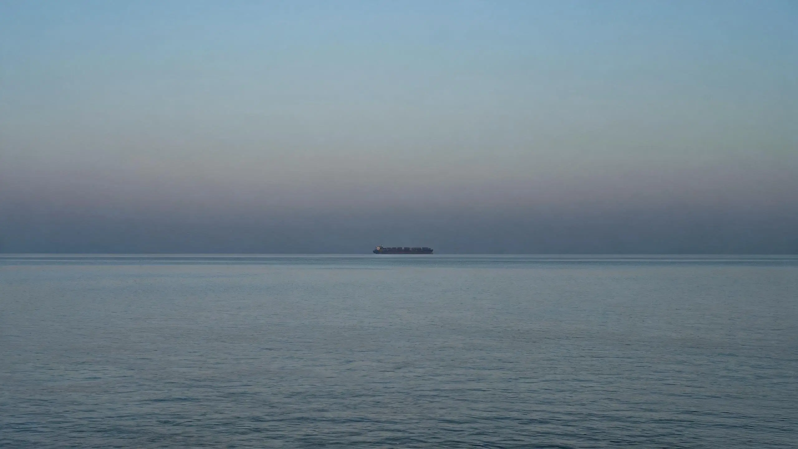 Ocean freight leg on the horizon Container ship on the ocean horizon at dusk, distant silhouette