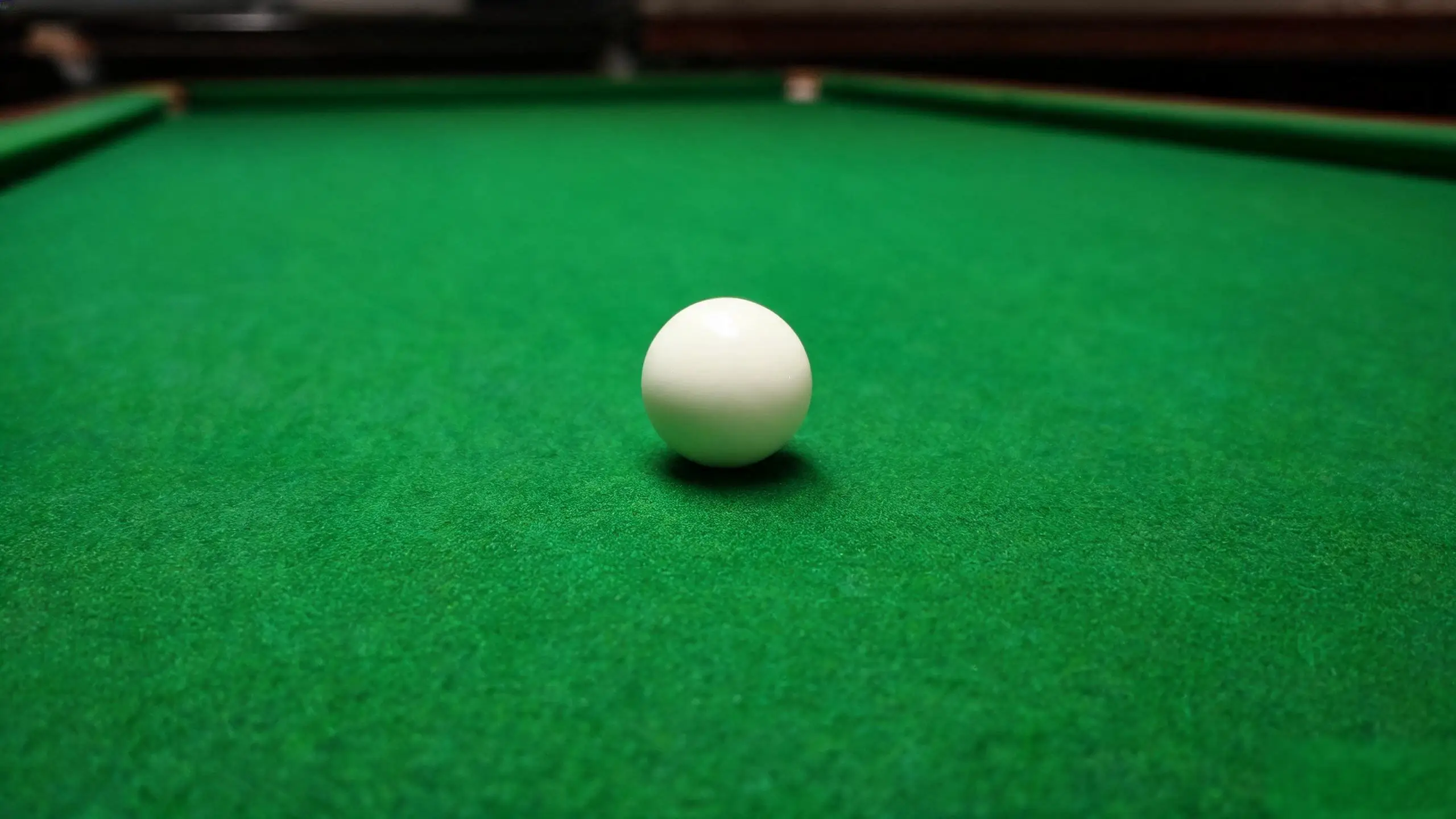 White cue ball on green billiard cloth, seen low along the line of a slow roll