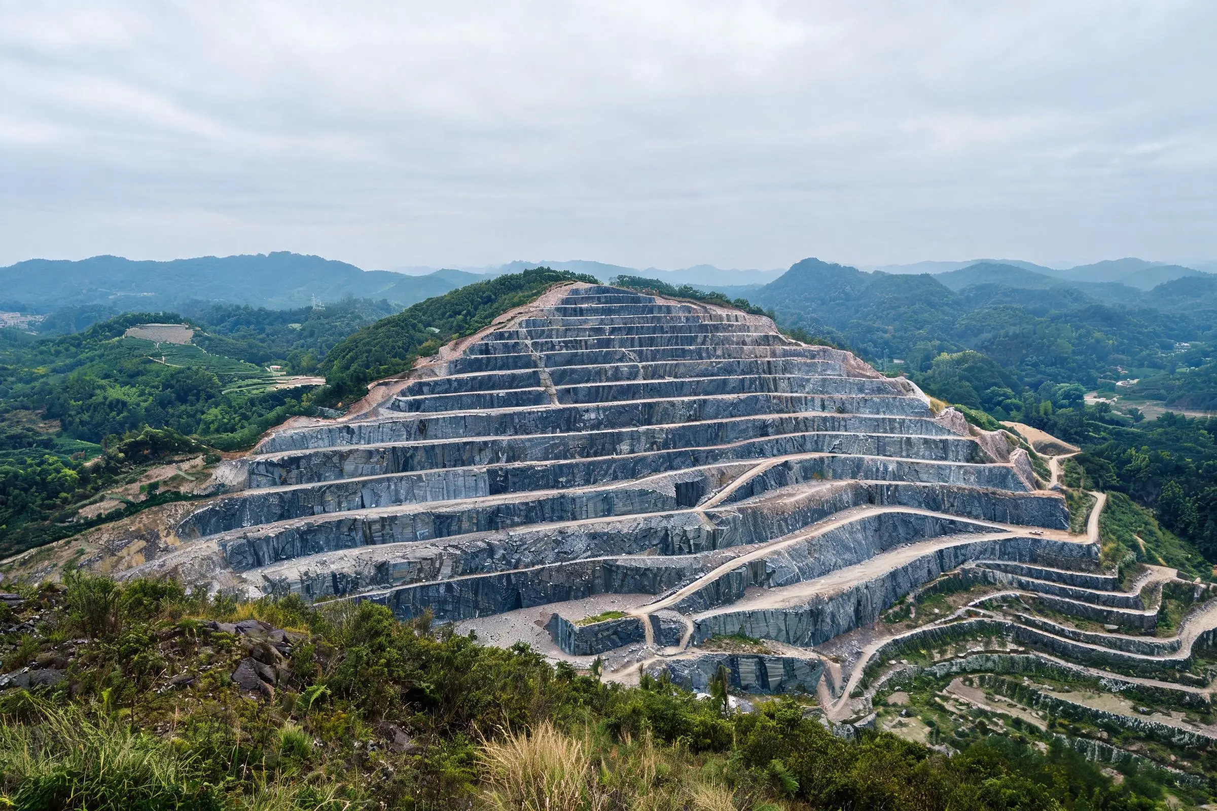 Bench method quarrying — stepped terraces in a Jiujiang slate quarry Aerial view of terraced slate quarry with stepped benches cut into a forested hillside