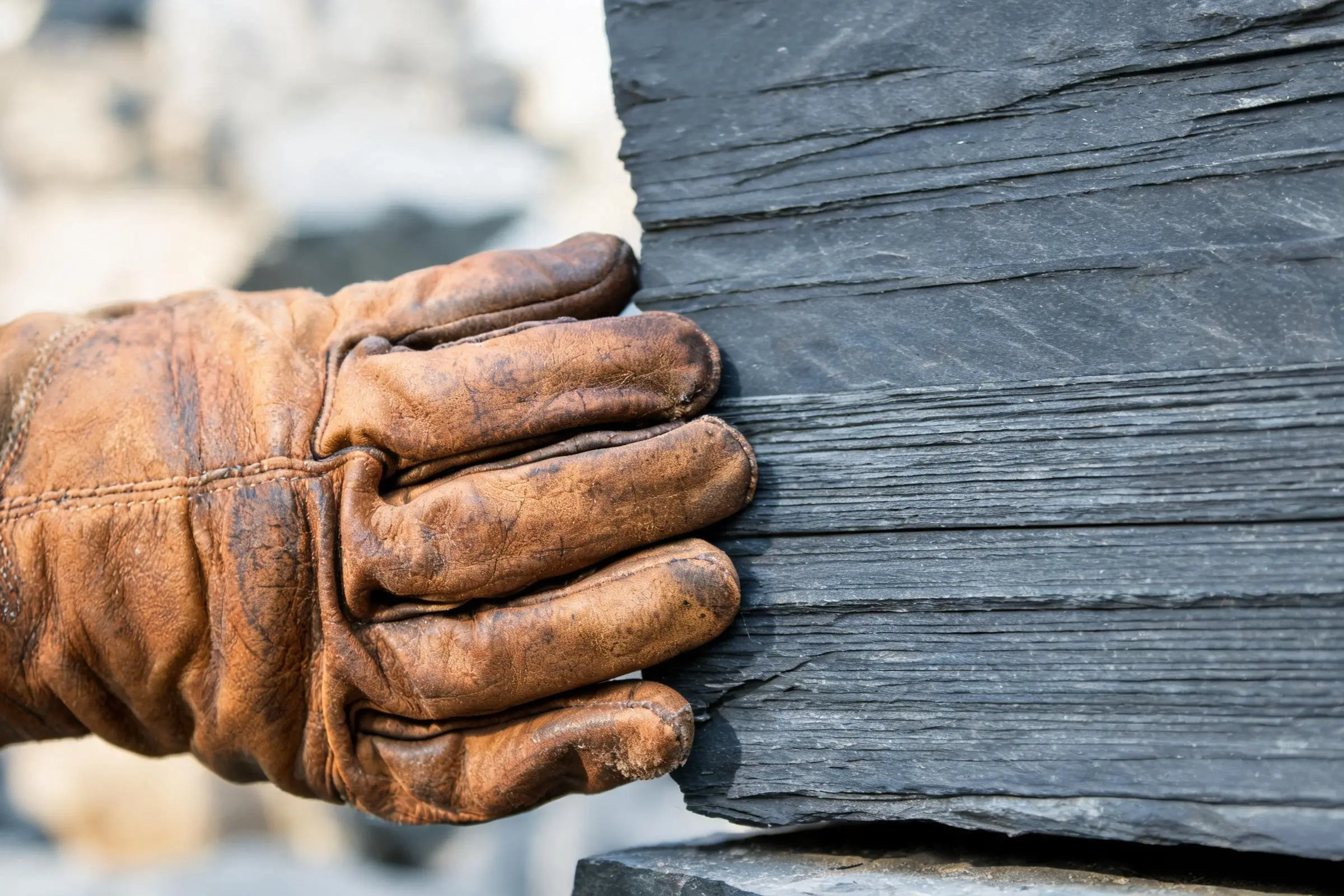 Testing slate cleavage direction by hand at the quarry face Quarry worker pressing gloved hand against slate block to test cleavage direction