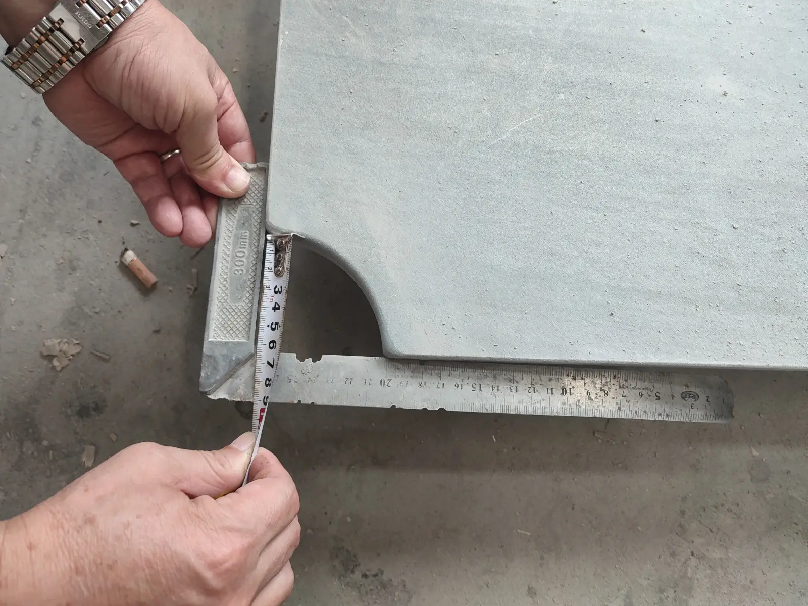 Worker using a straight edge and feeler gauge to check flatness of a dark grey slate panel during quality inspection