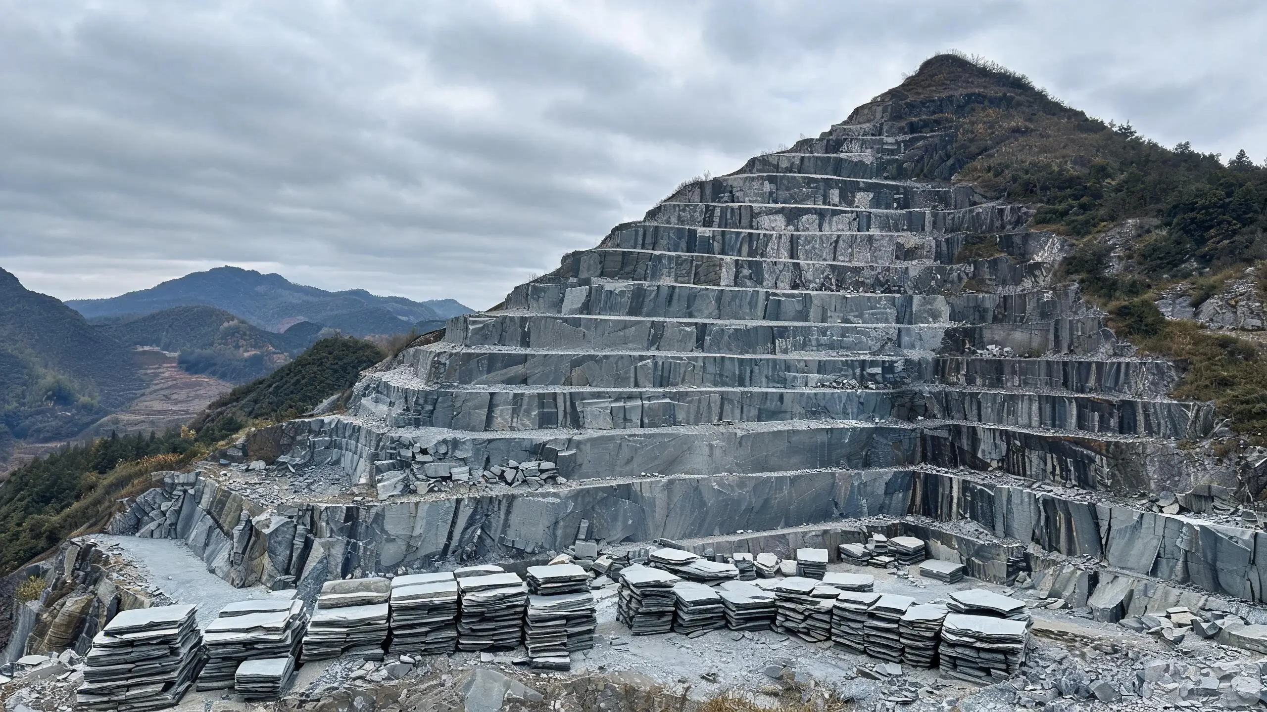 Open-pit slate quarry with stepped terraced working faces and extracted rectangular blocks at the base