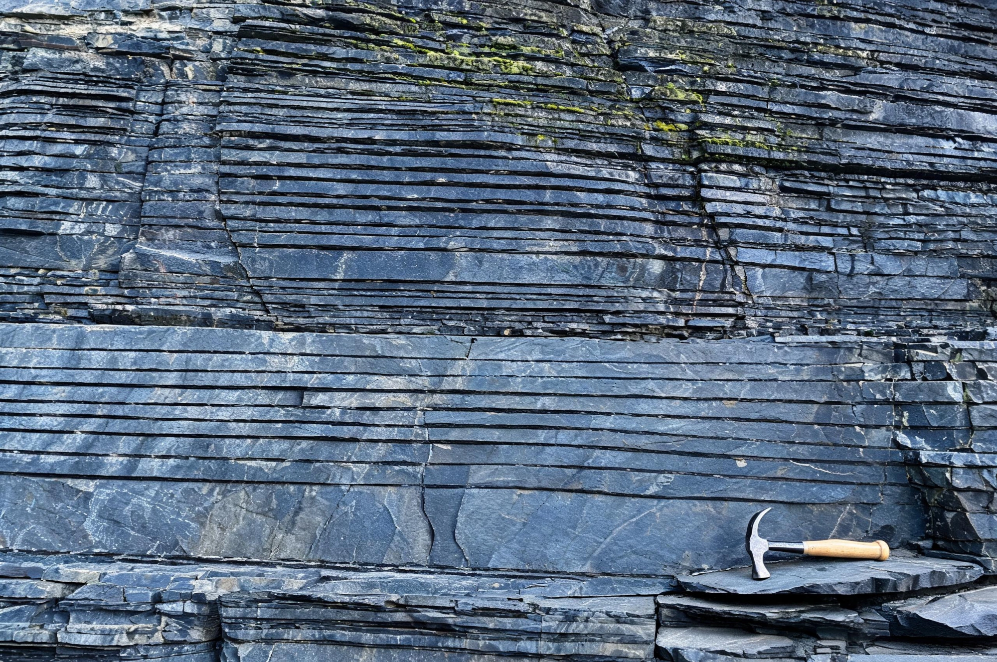 Jiujiang Slate Resources and Quarry Reserves 2 Close view of a slate quarry face showing thick grey-blue beds in cross-section, layers running straight and parallel like pages of a closed book