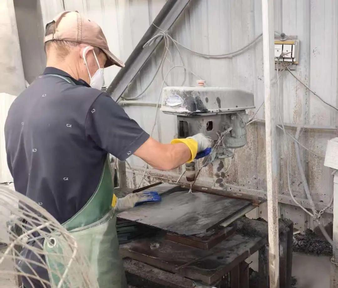 Hand-operated punch making a nail hole in a grey roofing slate tile