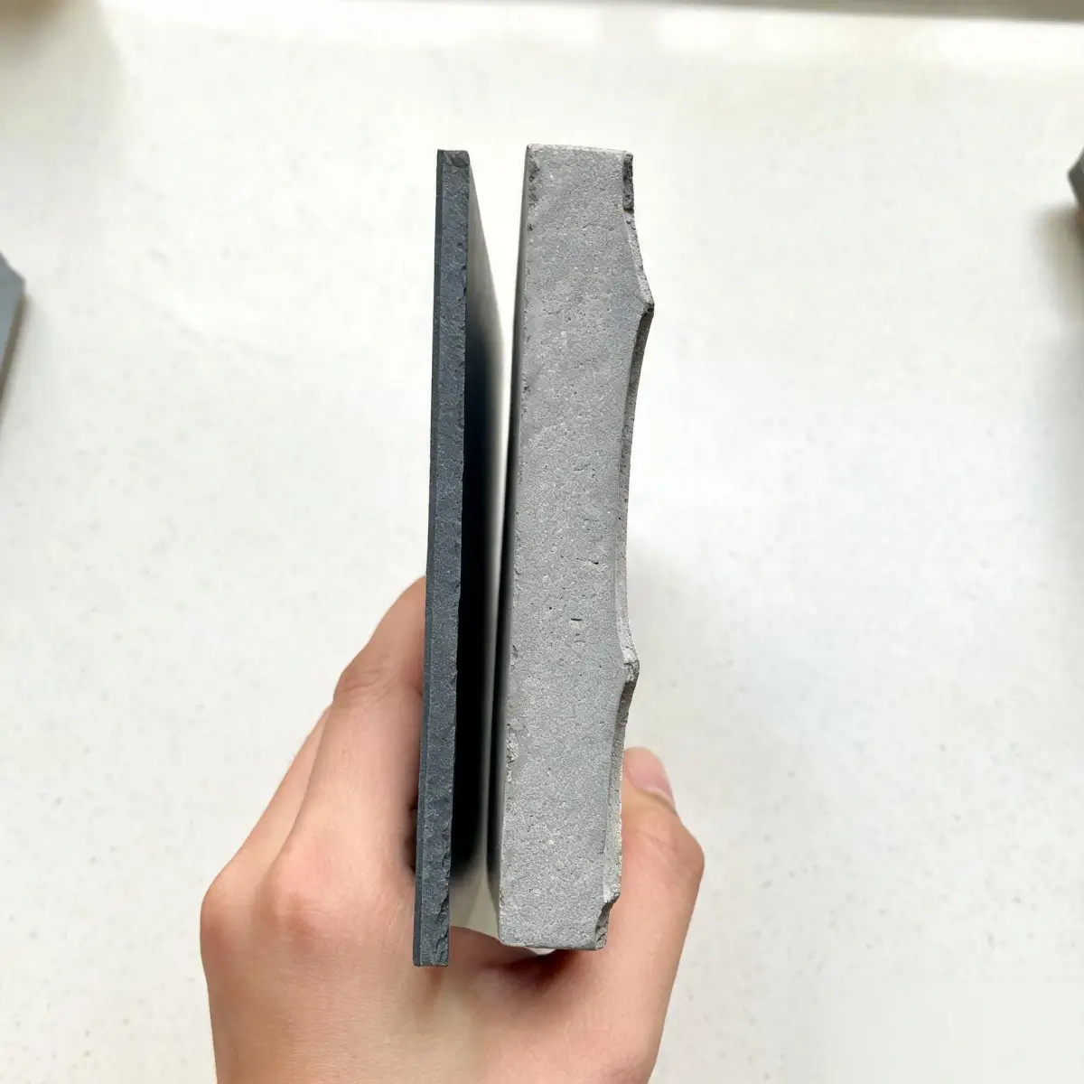 Myths About Natural Roofing Slate 3 Hand holding thin slate tile next to thick concrete tile showing weight comparison