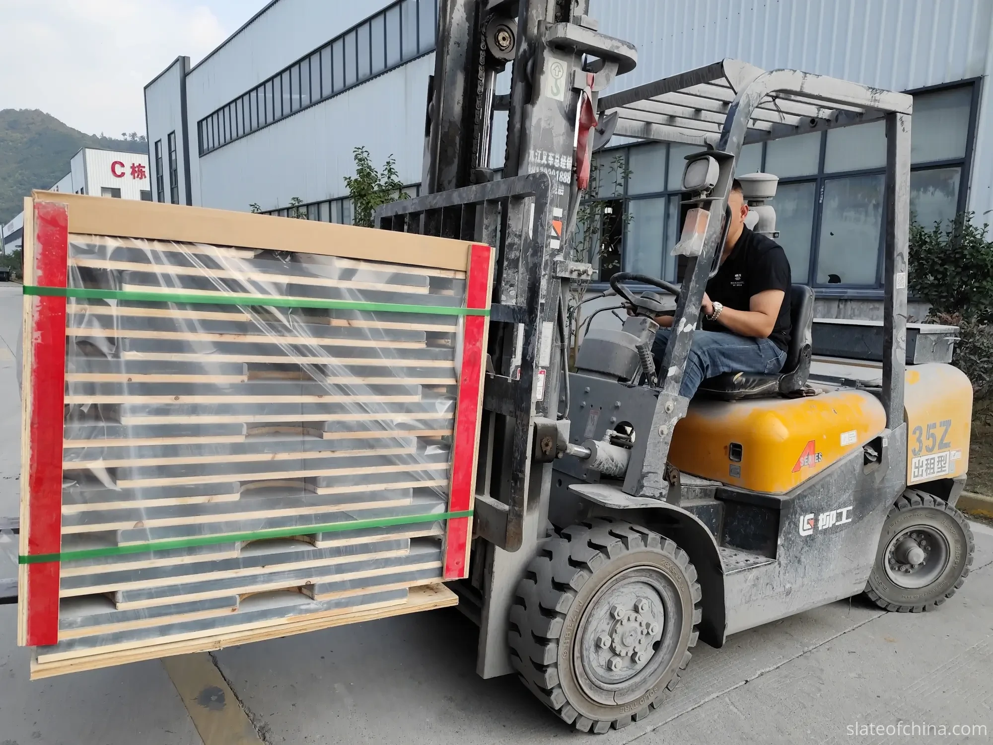 Export Wooden Crate Packing 5 Forklift lifting a palletized bundle of billiard slate panels wrapped in shrink film with green strapping and red edge guards in an industrial yard