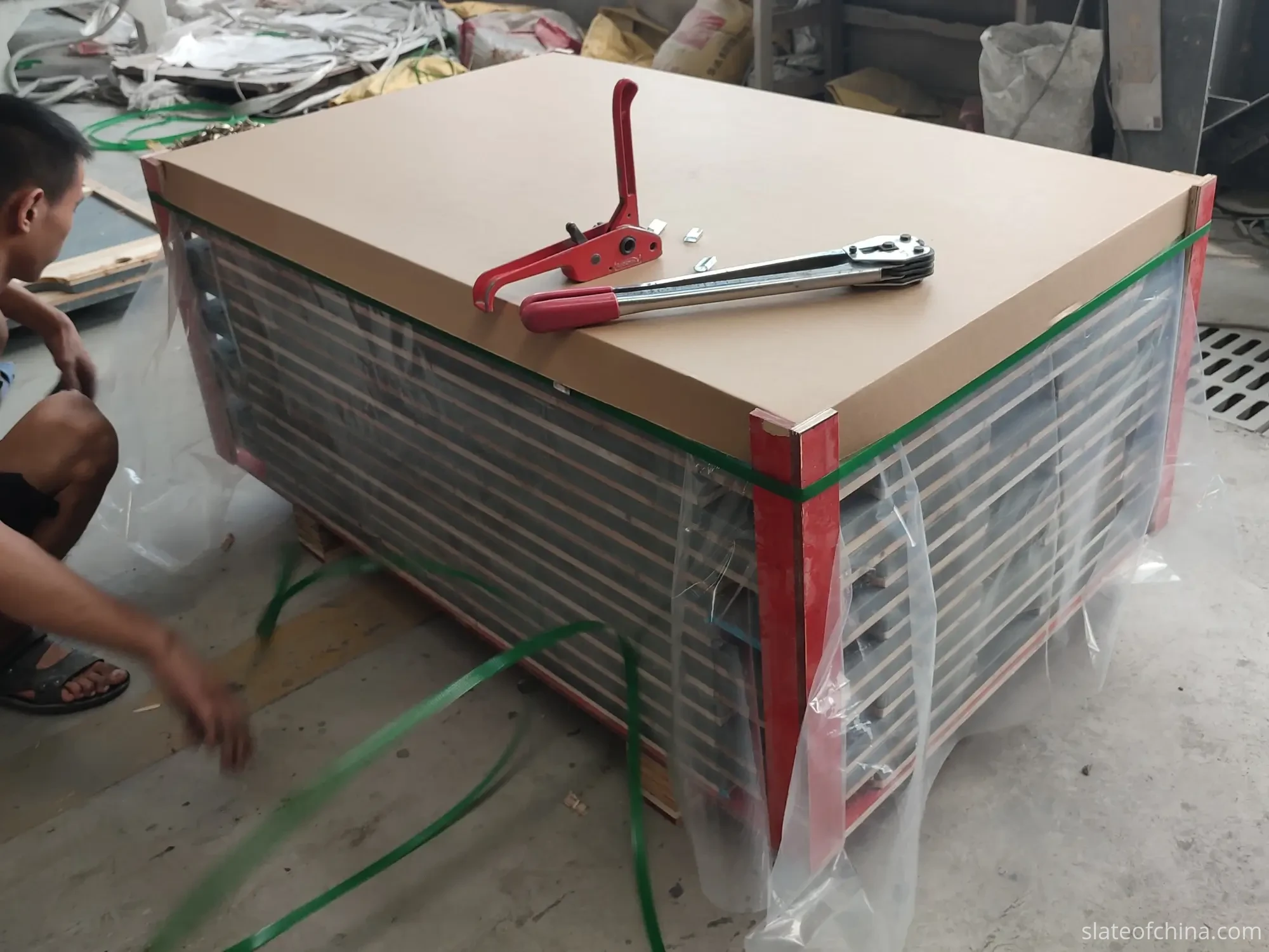 Billiard Slate Export Packing On A Wooden Pallet Packer securing strapping around a wrapped stack of billiard slate sets on a wooden pallet with corner protectors