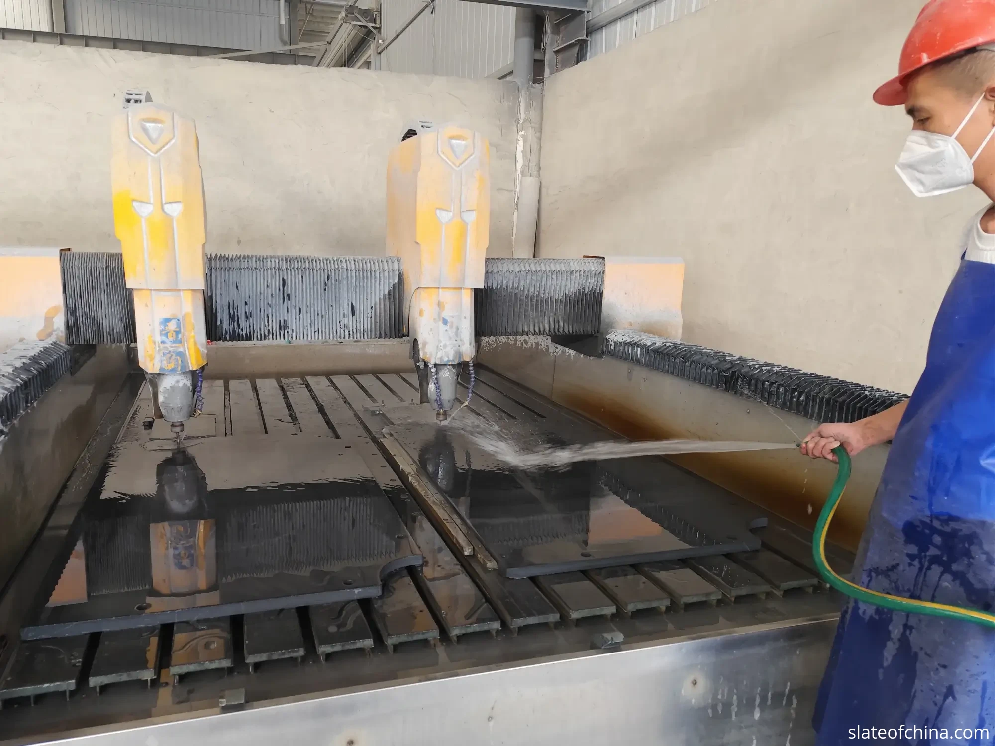 2026 Billiard Slate Industry Report 4 CNC machining station in a slate factory with a dual-head machine, a slate panel on the workbed and a worker flushing the surface with water