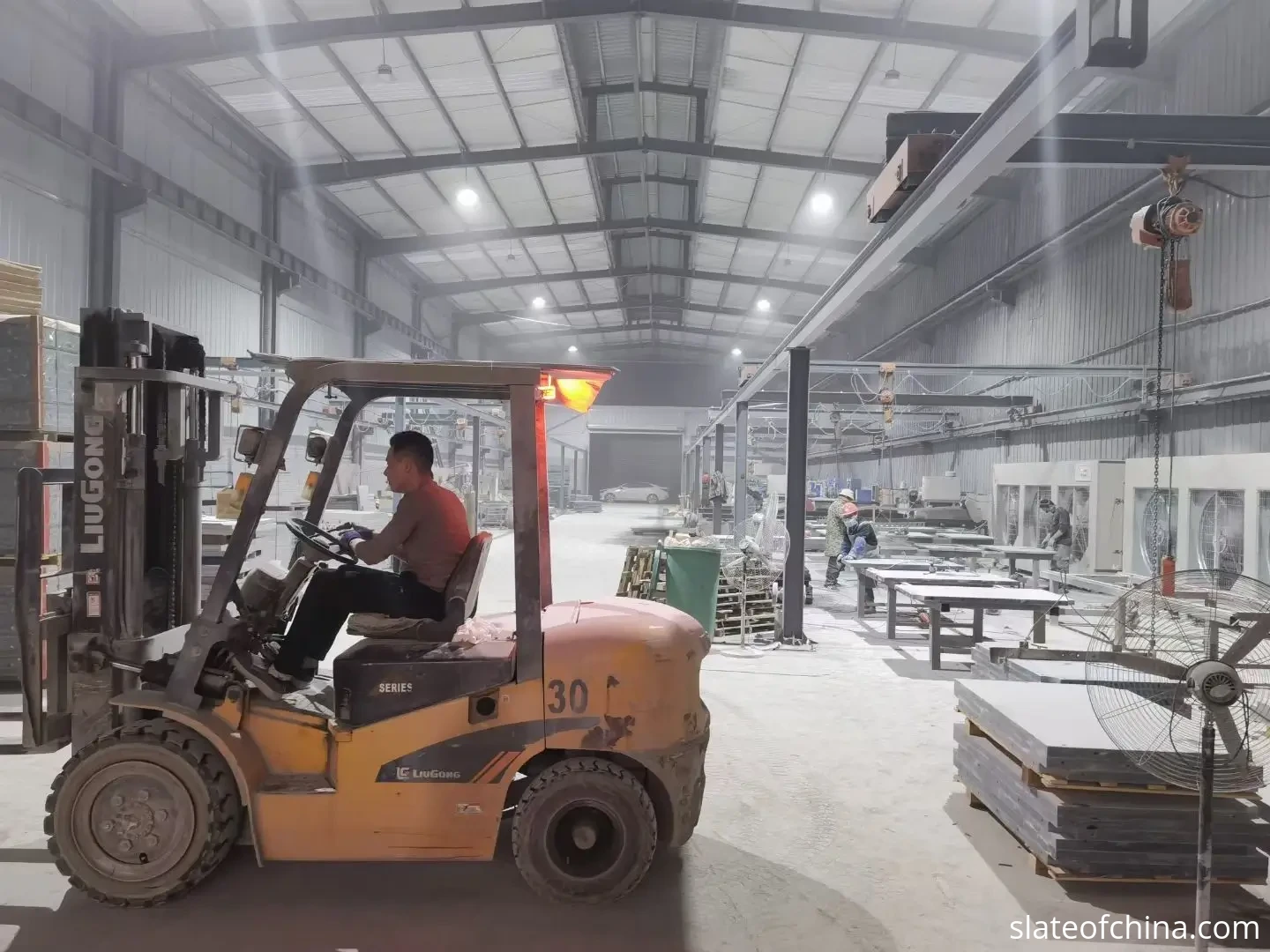 2026 Billiard Slate Industry Report 3 Slate processing factory floor with a forklift and grey slate panels on work tables under bright overhead lighting