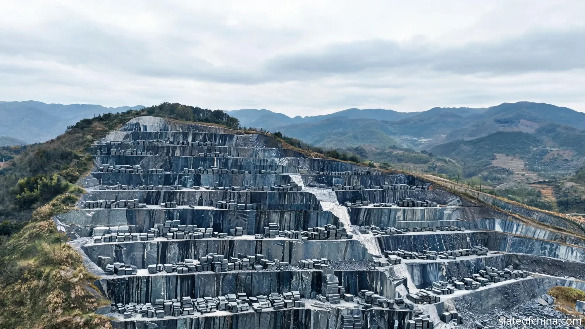 2026 Billiard Slate Industry Report 2 Terraced open-pit slate quarry in China with cut blocks stacked on stepped rock faces and mountains in the background