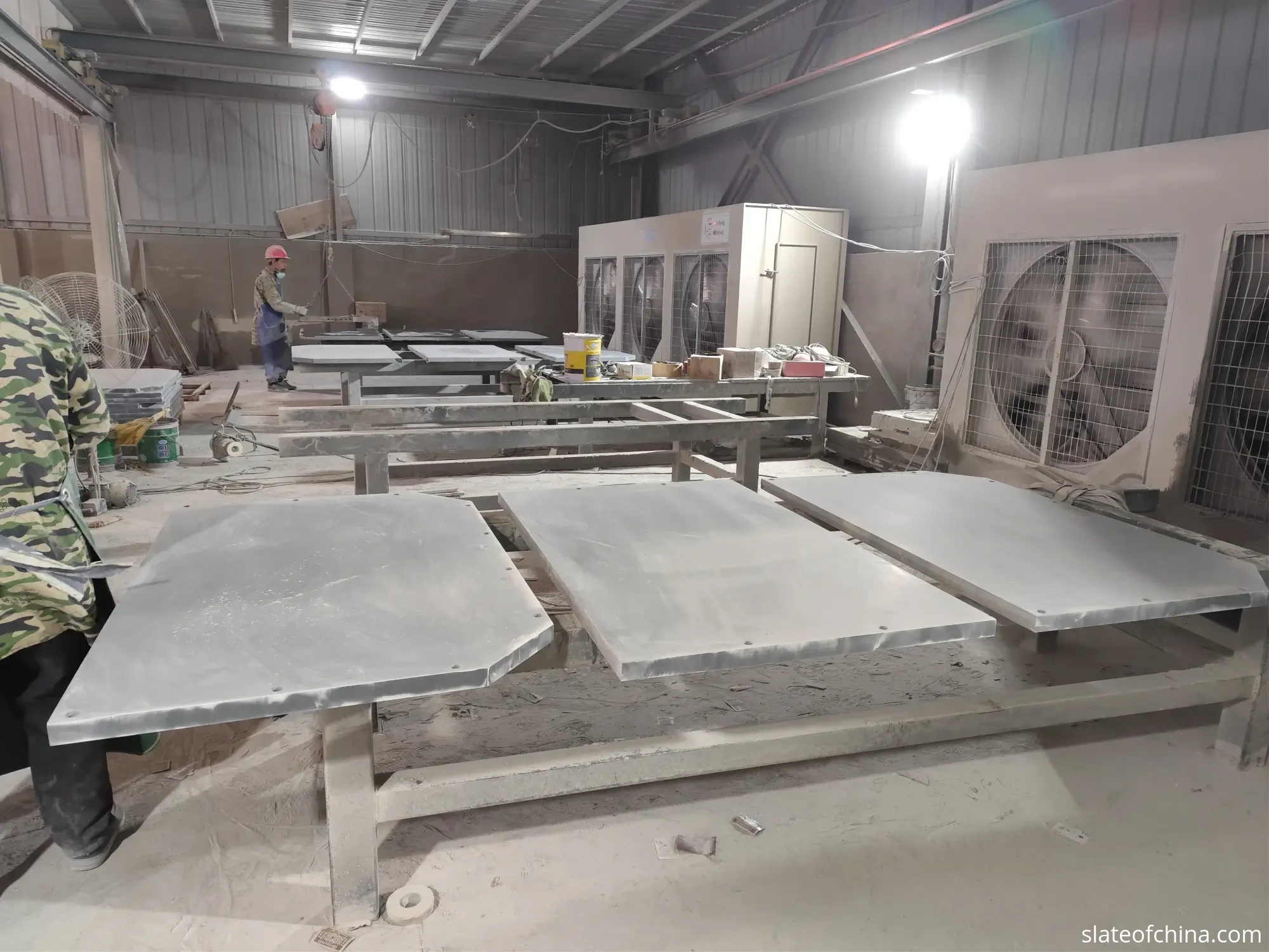 2026 Billiard Slate Industry Report 5 Finished grey slate panels with drilled holes and cut corners resting on wooden work racks in a slate workshop