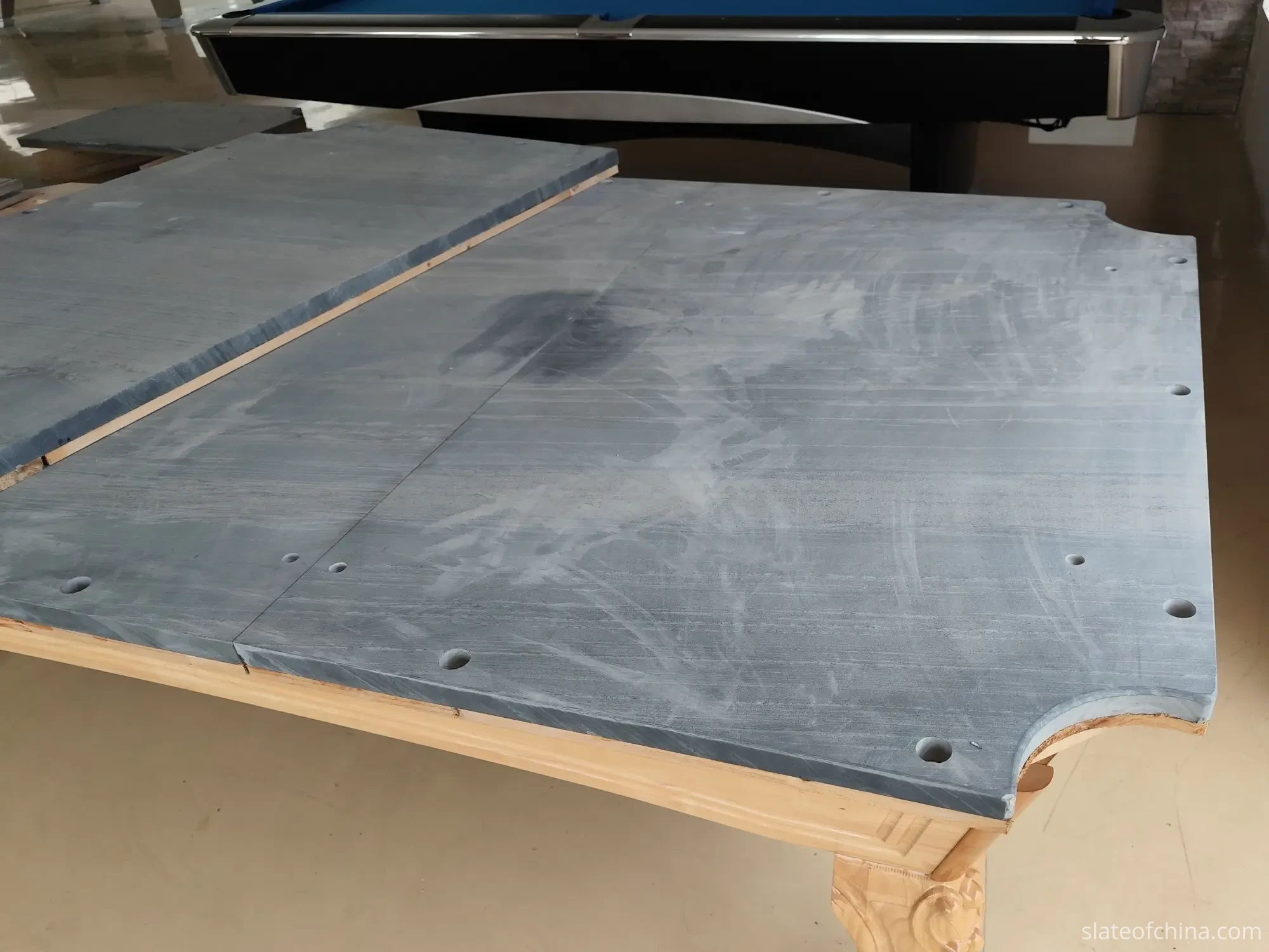 Billiard Slate Quality Control: What Buyers Should Check 1 Three-piece billiard slate bed test-assembled on a wooden pool table frame in a factory workshop, with a finished billiard table in the background