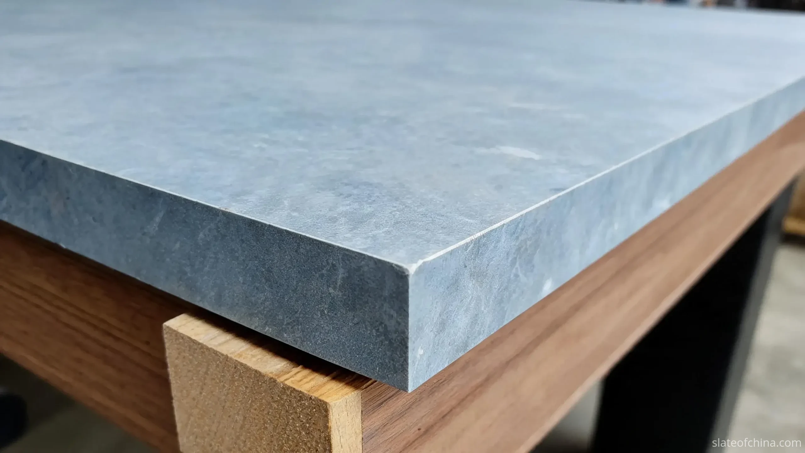 Thin pale wooden shim inserted at the corner support point between the underside of a blue-grey billiard slate panel and its wooden support block