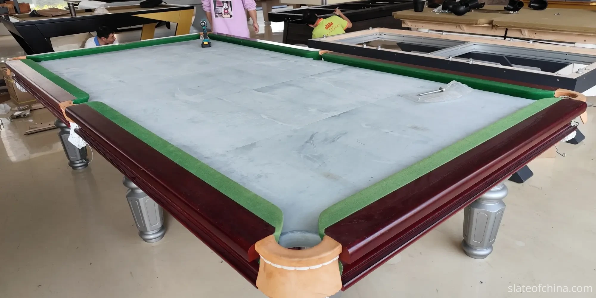 Billiard slate three-piece set with center joints visible Three-piece billiard slate set installed in a table frame on the factory floor, showing the two center joints where the panels meet