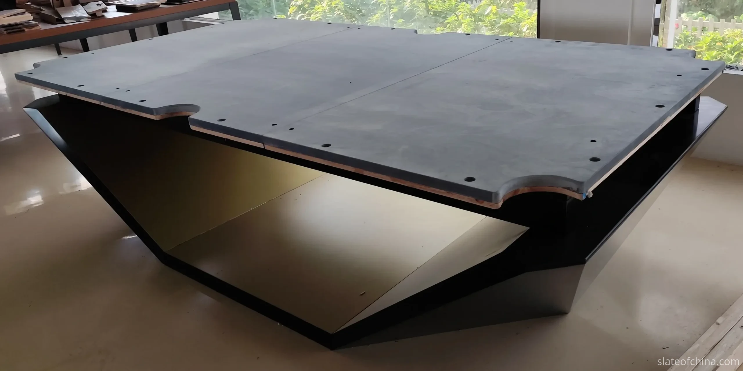 Three-piece slate bed assembled on a black and gold billiard table base, two straight seams across the bed with countersunk mounting holes and pocket cutouts visible
