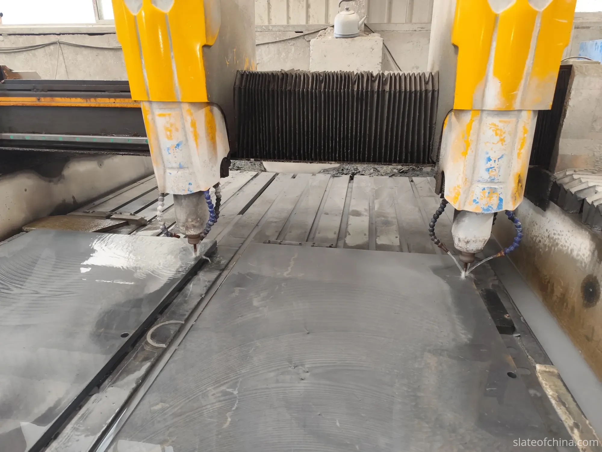 CNC Machining Billiard Slate With Dual Spindles Dual-spindle CNC machining center working over two wet slate slabs in a stone workshop, coolant dispensing at the spindle tips with pre-drilled holes visible