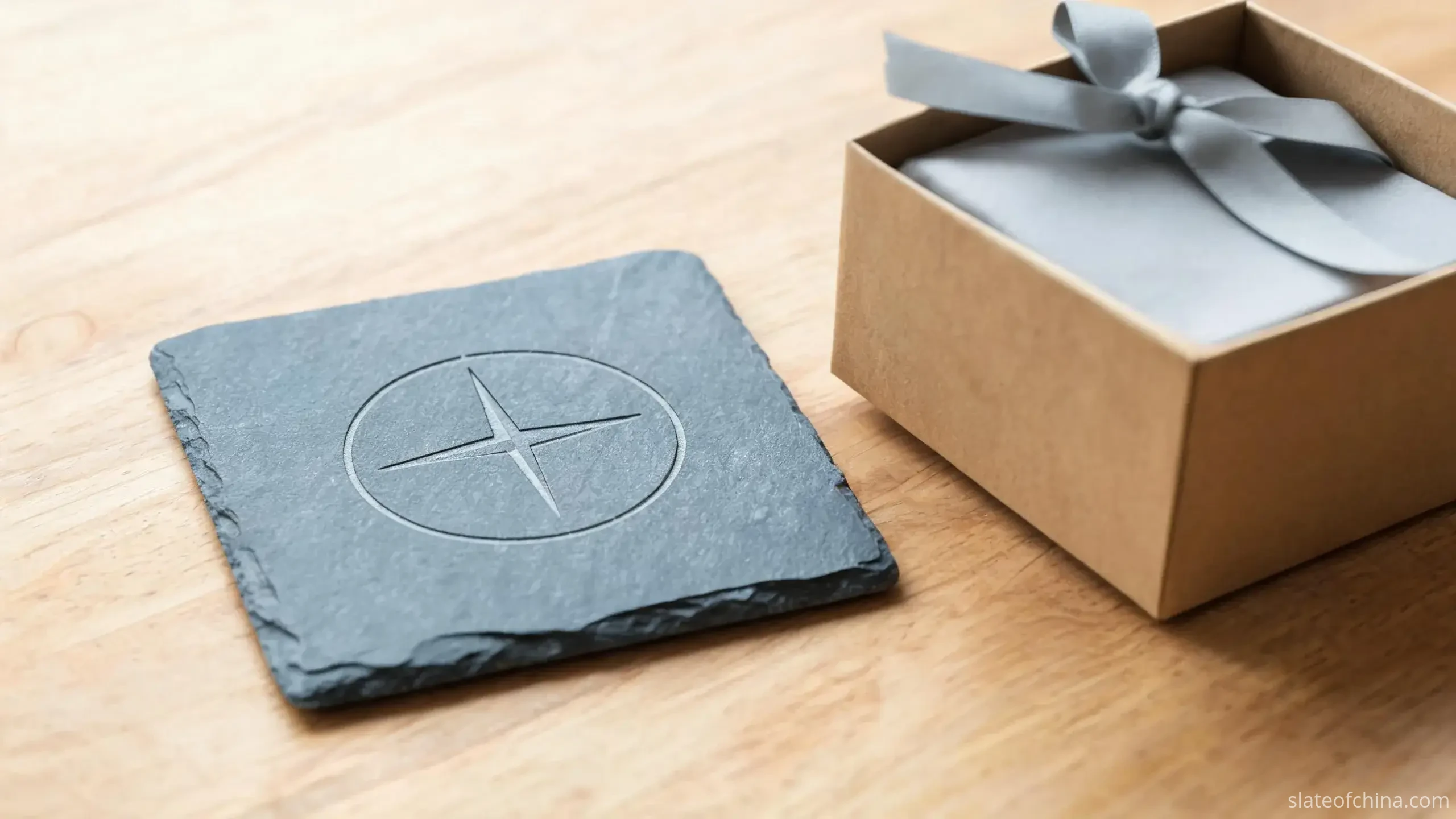 Slate Coasters from Jiujiang 3 Illustrative coaster with an engraved geometric emblem beside an open kraft gift box with a grey paper sleeve