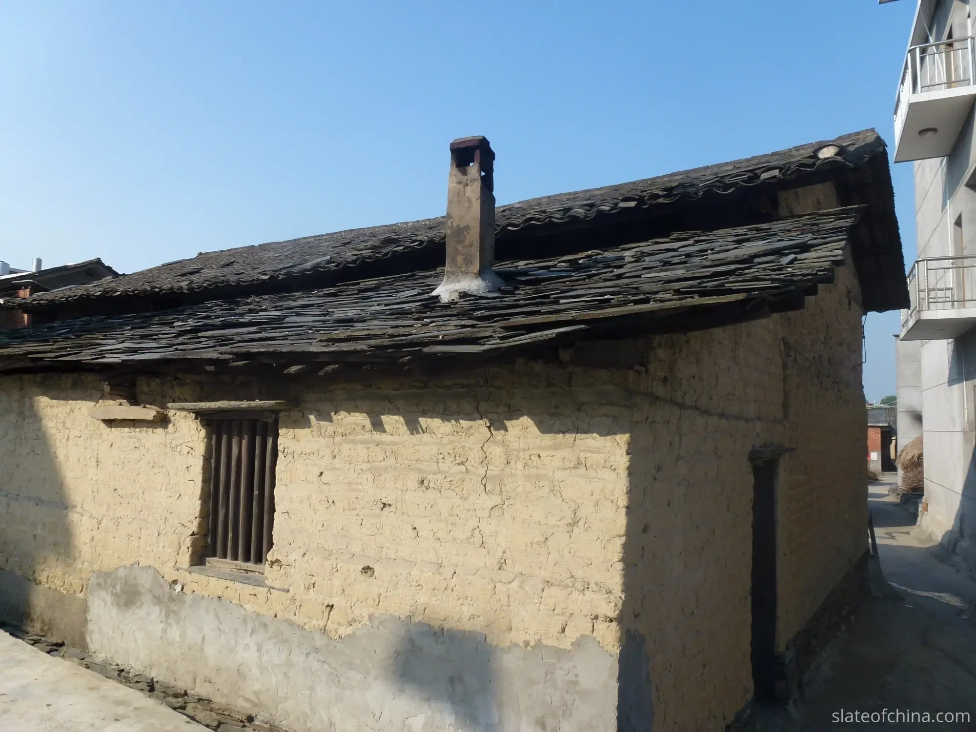 Slate roofs on old village houses near the hills of northern Jiangxi, weathered tiles in graduated blue-grey tones, a few newer tiles darker than their neighbours