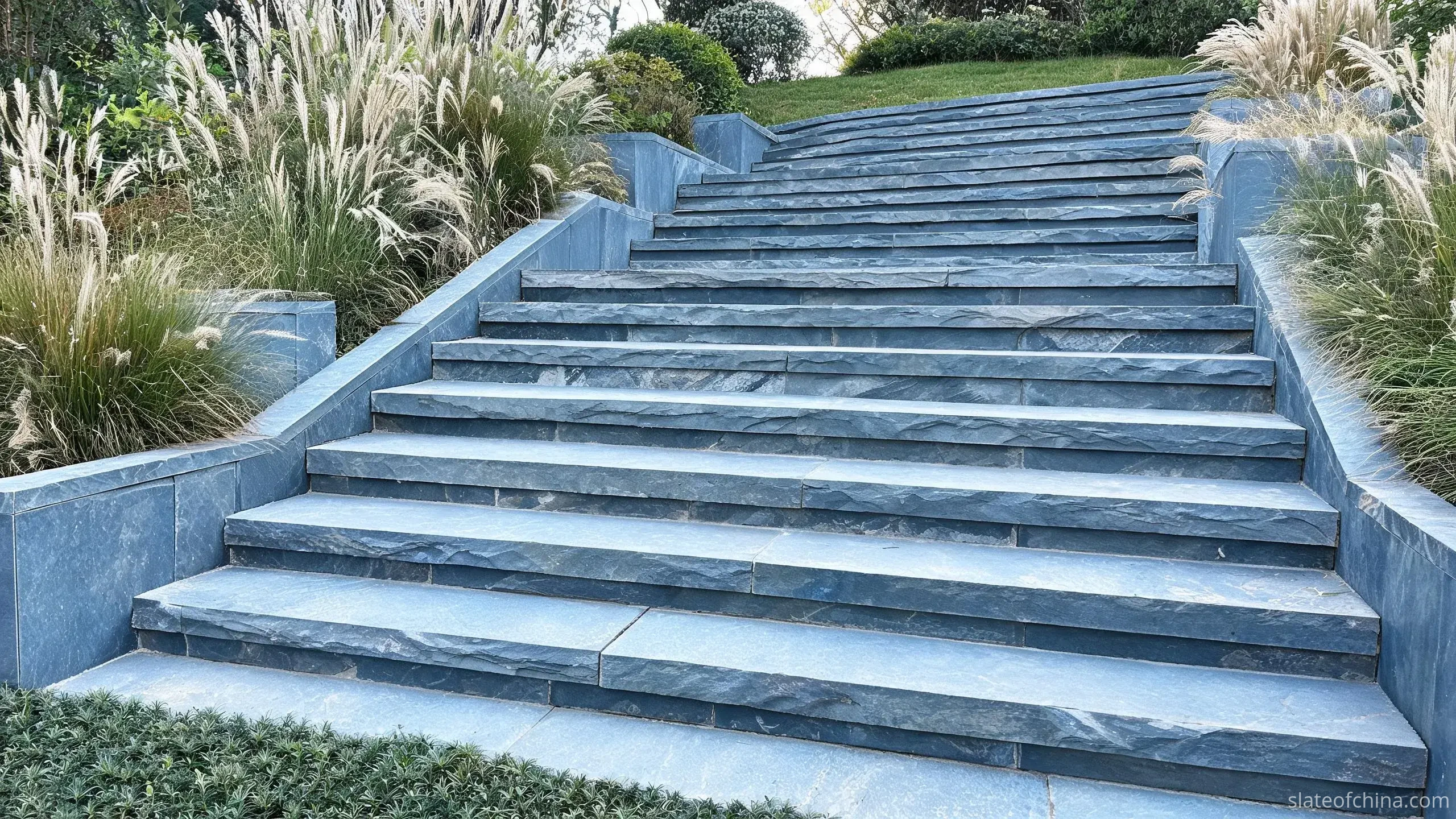 Jiujiang Slate for Outdoor Architecture 3 Illustrative view of an outdoor slate staircase with solid blue-grey treads and risers, grasses planted beside low slate cheek walls
