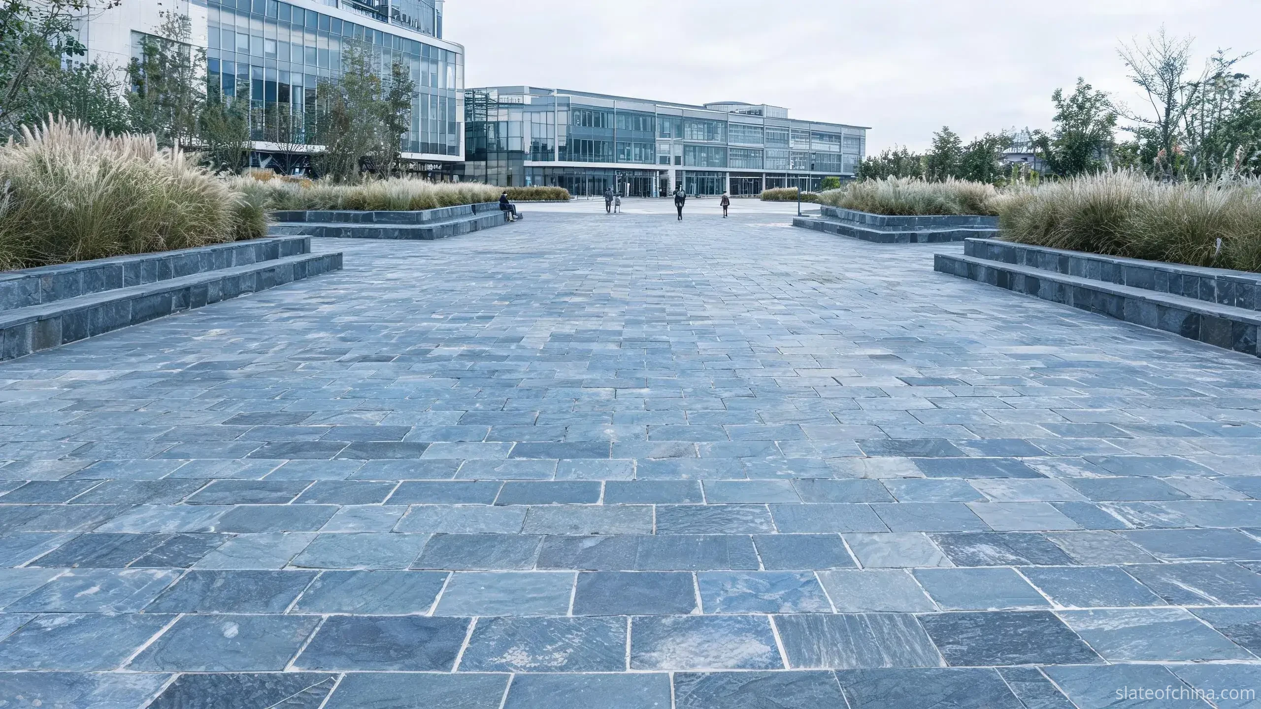Jiujiang Slate for Outdoor Architecture 1 Illustrative view of large-format cool blue-grey slate paving laid on a shaded public plaza, running bond pattern with narrow sawn joints and low slate seat walls