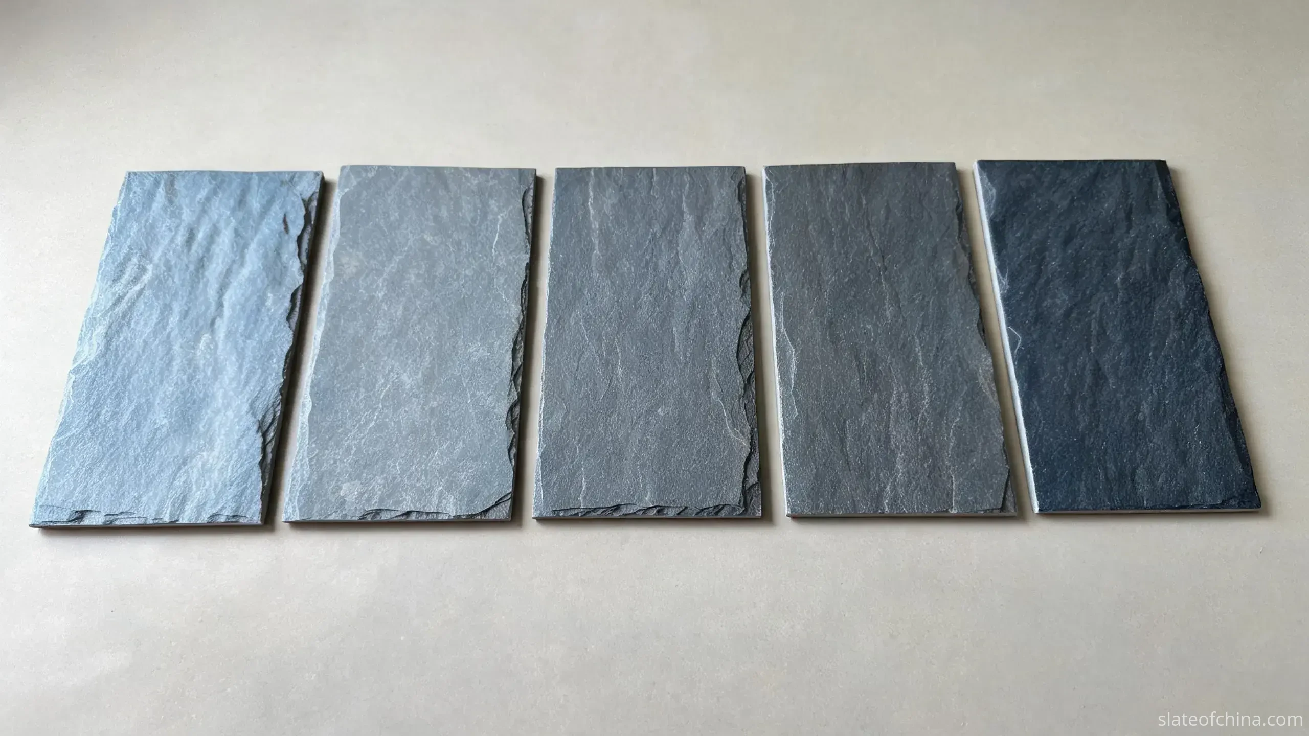 Jiujiang Slate Wall Cladding 3 Row of slate wall cladding samples ranging from lighter blue-grey through mid grey to deep charcoal, cool muted tones on a neutral surface