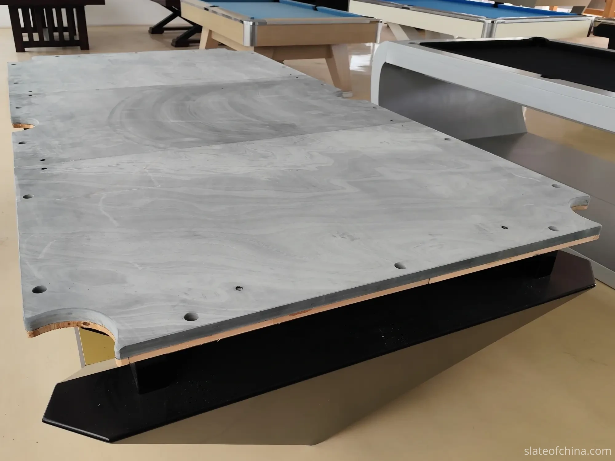 Bare three-piece grey slate bed assembled on a pool table frame in a bright workshop, ready for precision leveling