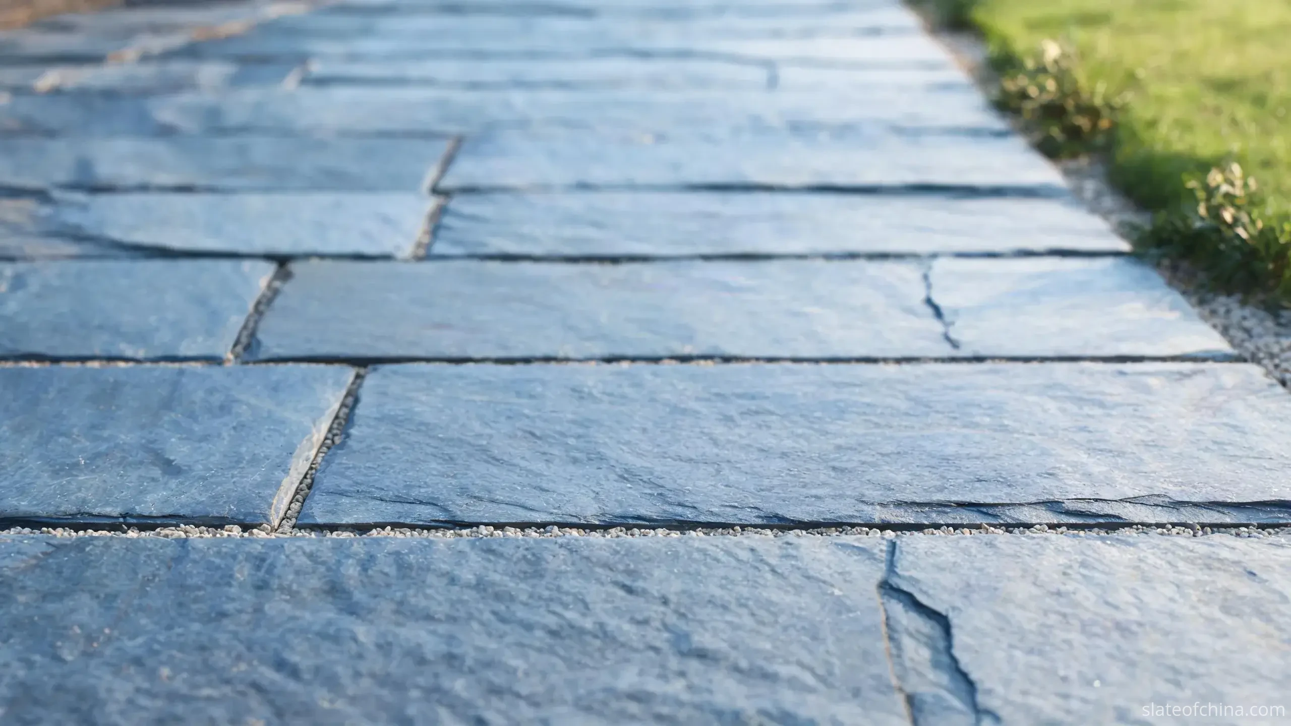 Why Jiujiang Slate Works for Paving 1 Close grazing-angle view across dry natural cleft slate paving in soft raking light, rectangular blue-grey flags in running bond with fine gravel joints, shallow relief catching faint micro-shadows