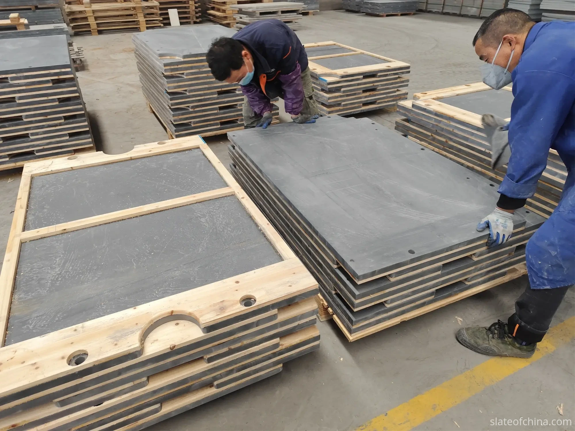 OEM Billiard Slate Manufacturing Process 1 Finished billiard slate sets stacked on wooden pallets in the factory warehouse, two workers inspecting and wiping panel surfaces before packing