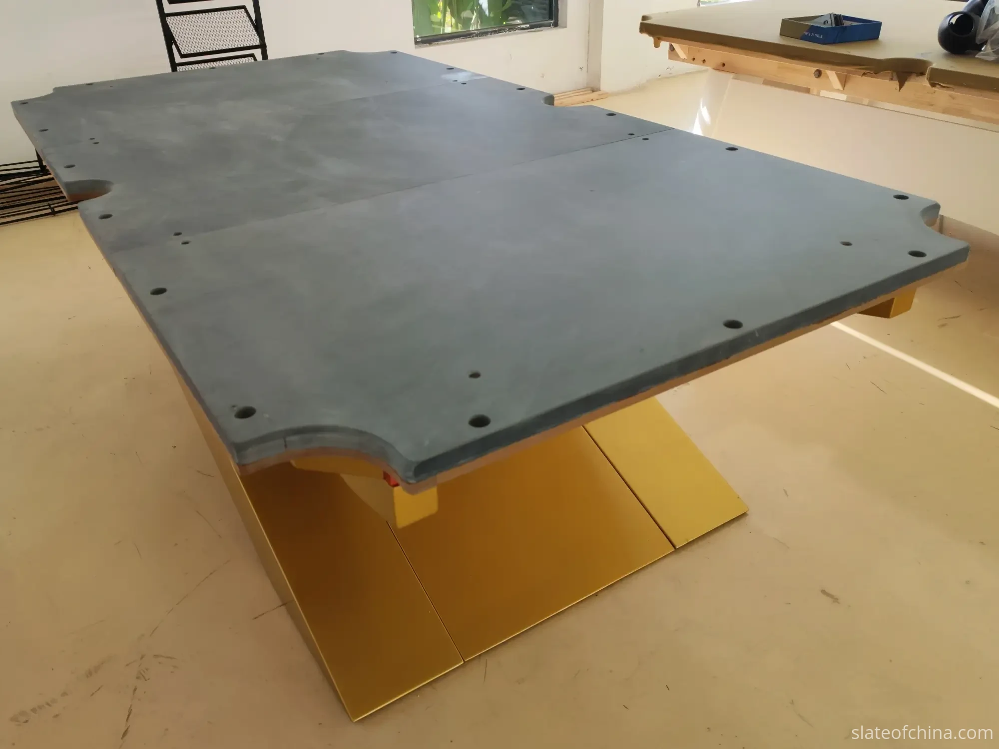 OEM Billiard Slate Manufacturing Process 2 Three-piece billiard slate bed mounted on a yellow metal support frame in the factory, two straight seams visible across the width, pre-drilled mounting holes along the shaped edges