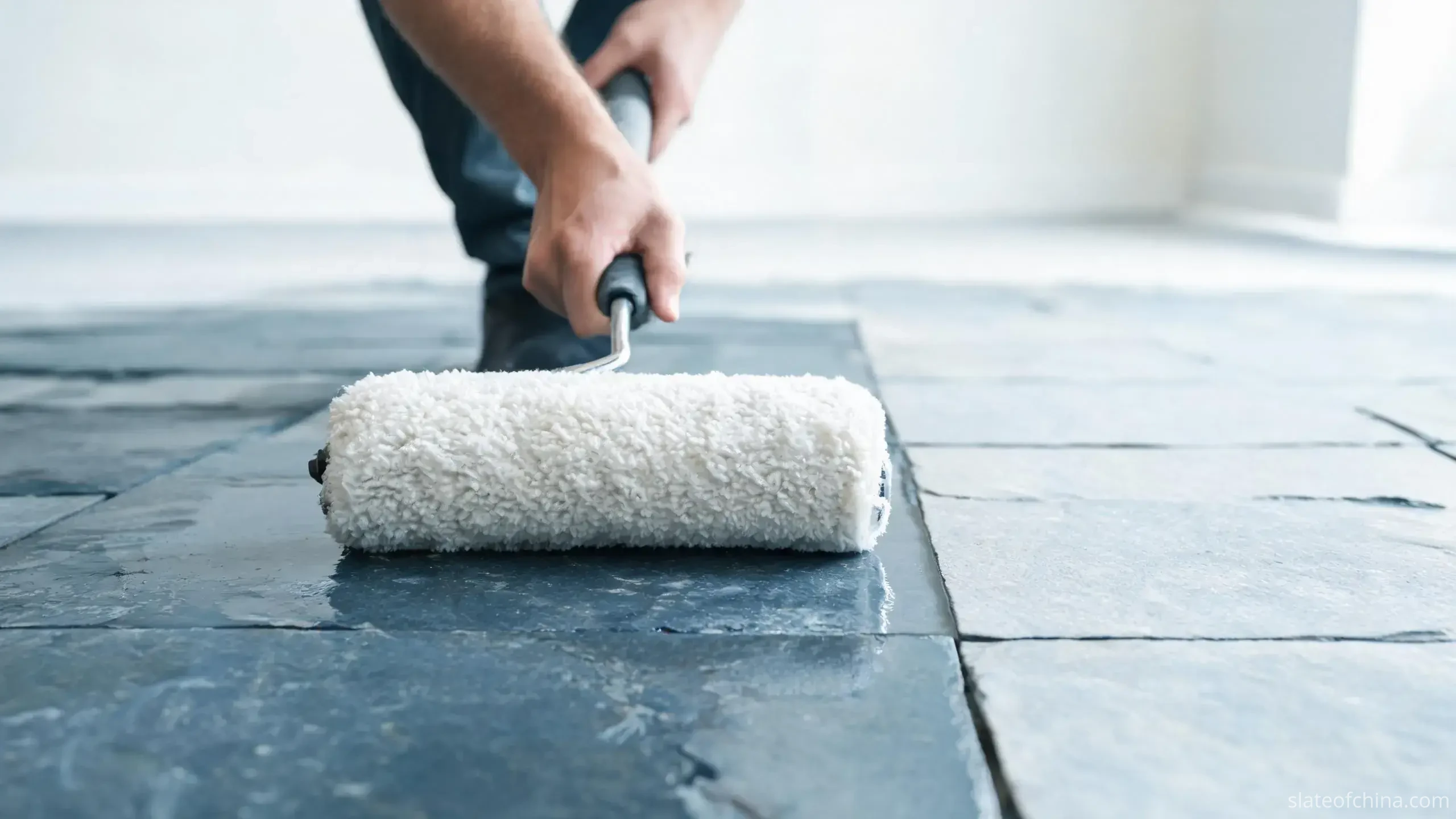 Slate Flooring vs Other Stone Flooring 3 Worker applying clear penetrating sealer to a blue-grey slate floor with a lambswool applicator, treated area slightly deepened in tone beside the untreated section