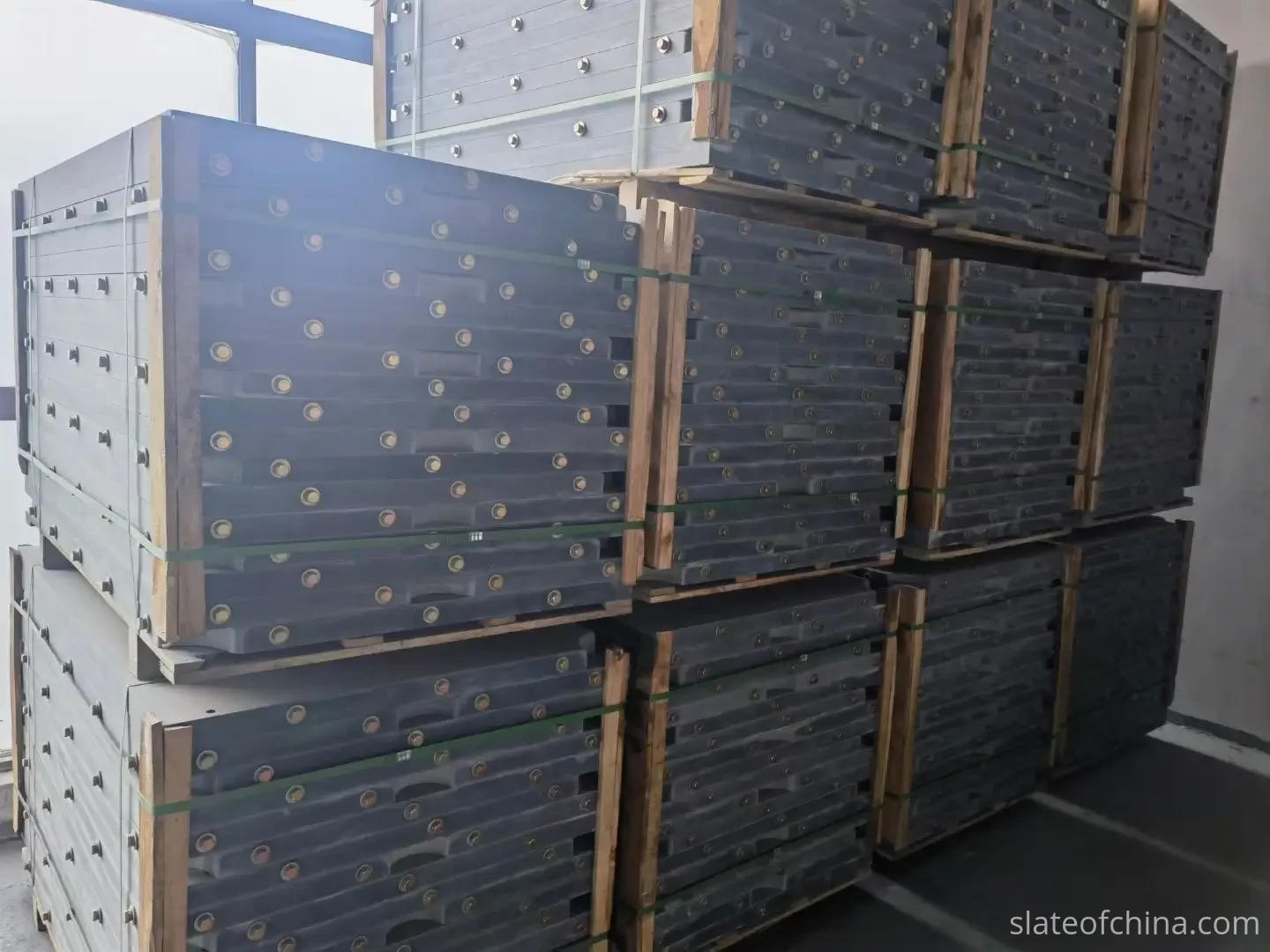How Slate Flatness Affects Ball Roll 6 Stacks of pre-drilled billiard slate panels bundled with timber bracing and strapping, stored three tiers high on wooden pallets in a warehouse