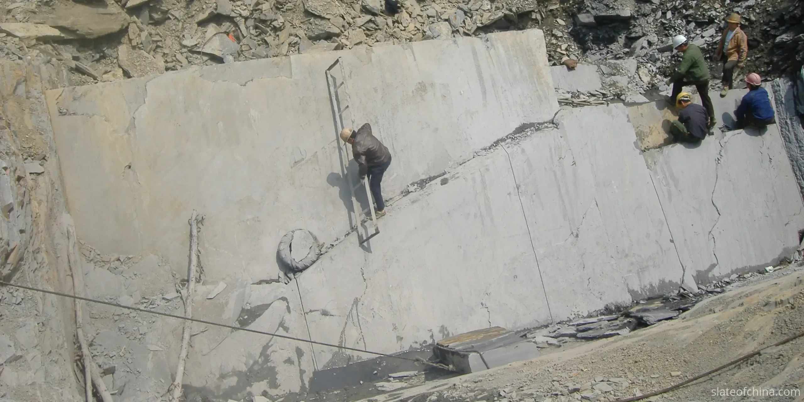 Slate Quarries and Processing in Jiujiang 1 Slate quarry working face with undulating natural bedding, five crew members in helmets on the bench and rough rubble below