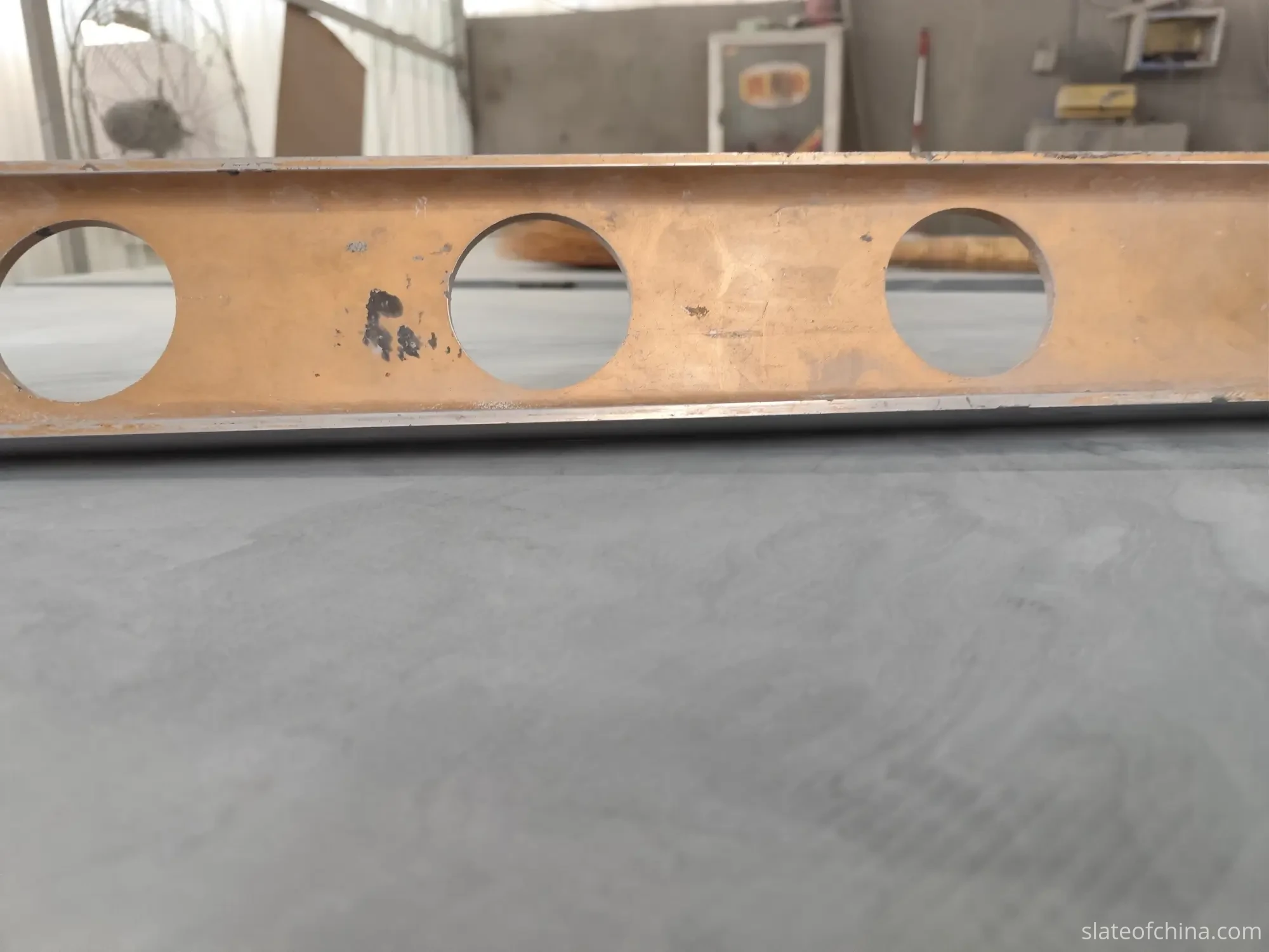 How Slate Flatness Affects Ball Roll 2 A precision straightedge resting across a grey honed billiard slate surface during a flatness check in a stone fabrication workshop